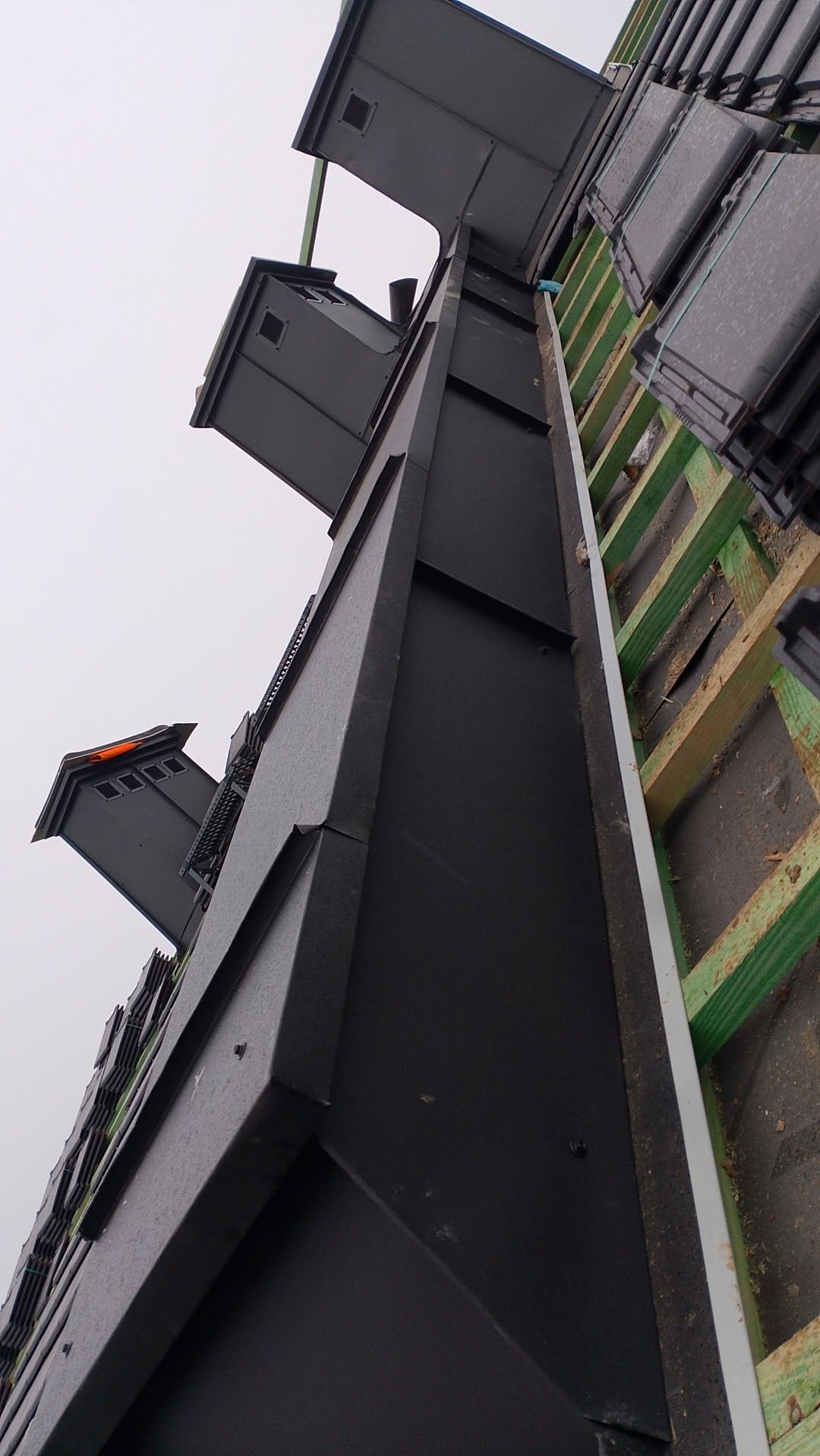 Nowoczesny dach z czarną blachą trapezową i elementami wentylacyjnymi, widok z dołu, ukazujący konstrukcję i detale wykończenia.