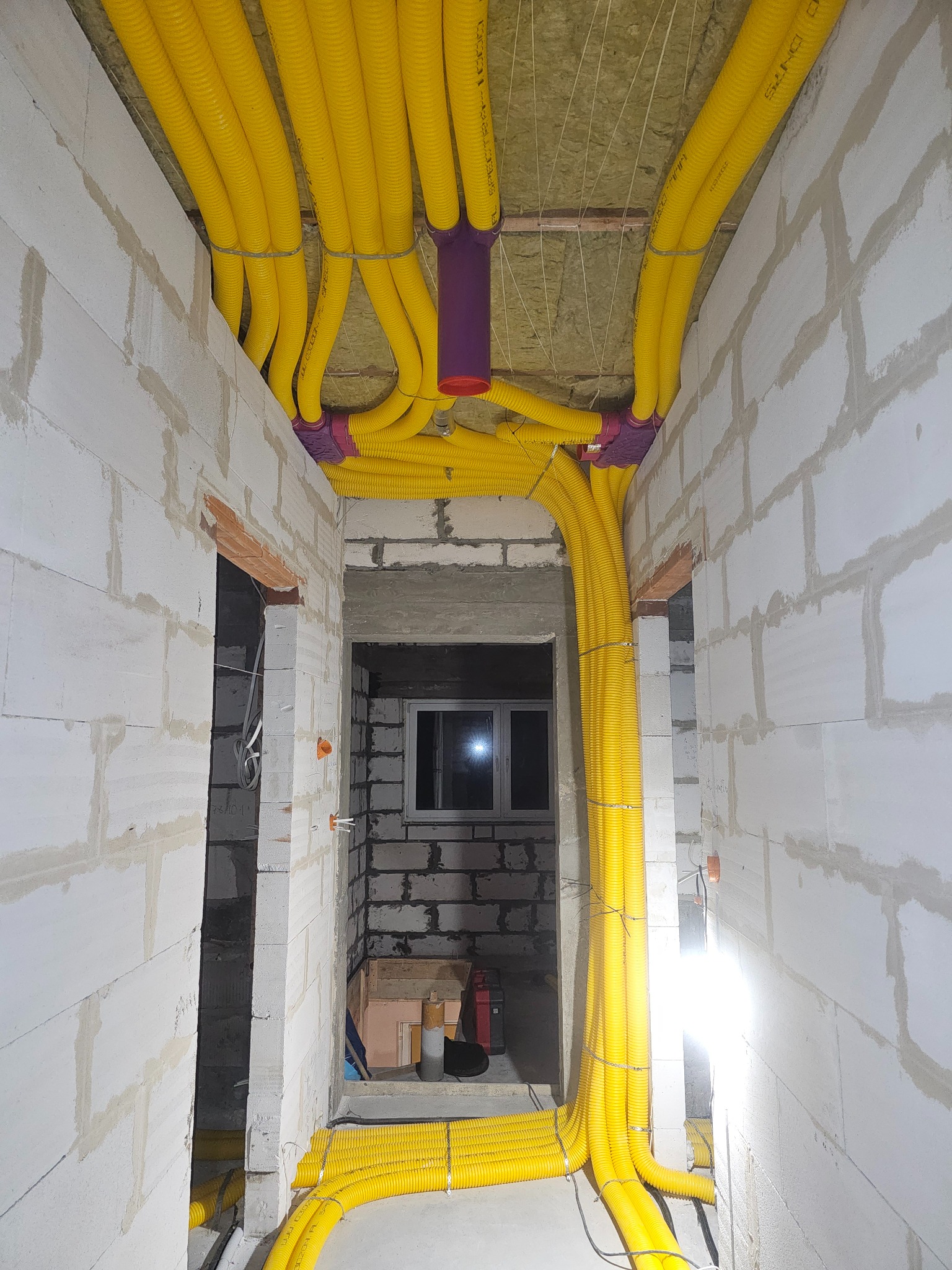 Żółte, elastyczne przewody wentylacyjne Spectra 1000 doprowadzone do fioletowych rozdzielaczy systemu rekuperacji Max Vent w surowym wnętrzu budynku z białych bloczków.