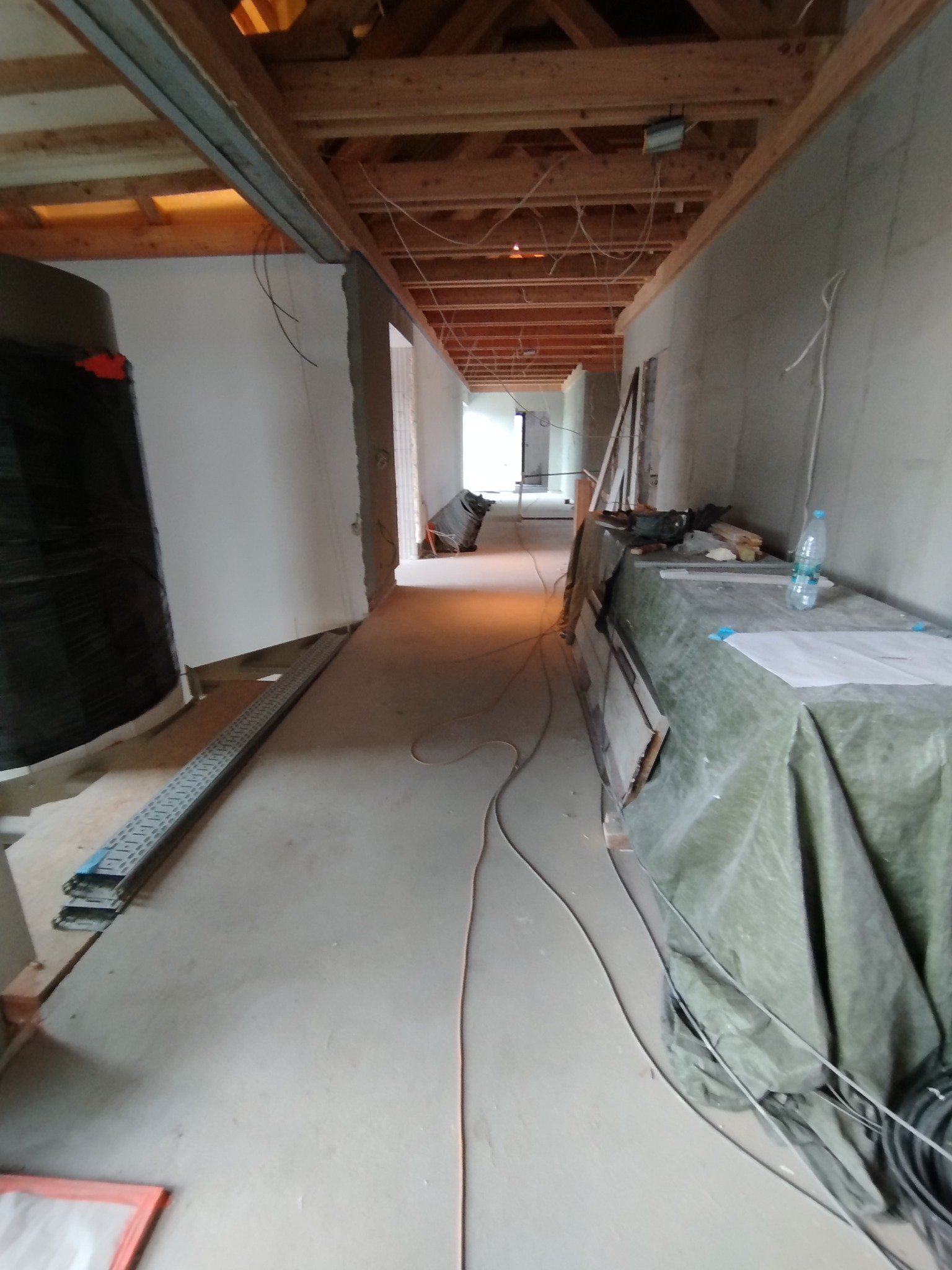 Wnętrze w trakcie prac wykończeniowych: surowy stan, widoczne instalacje pod sufitem, zabezpieczone powierzchnie, przygotowania do dalszych etapów prac.