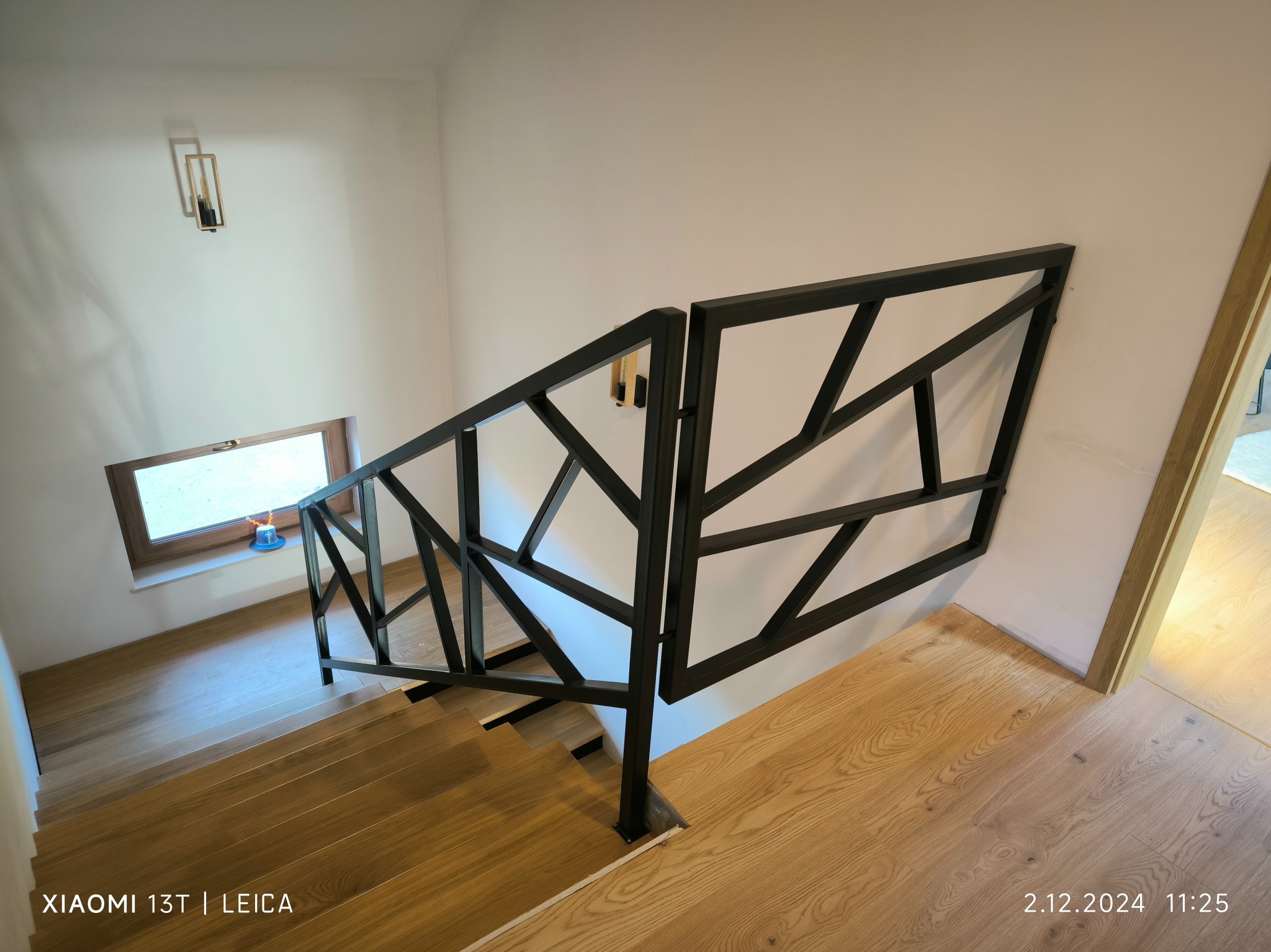 Nowoczesna, geometryczna balustrada schodowa w czarnym kolorze, zamontowana na drewnianych schodach. Widok z góry, oświetlenie naturalne.