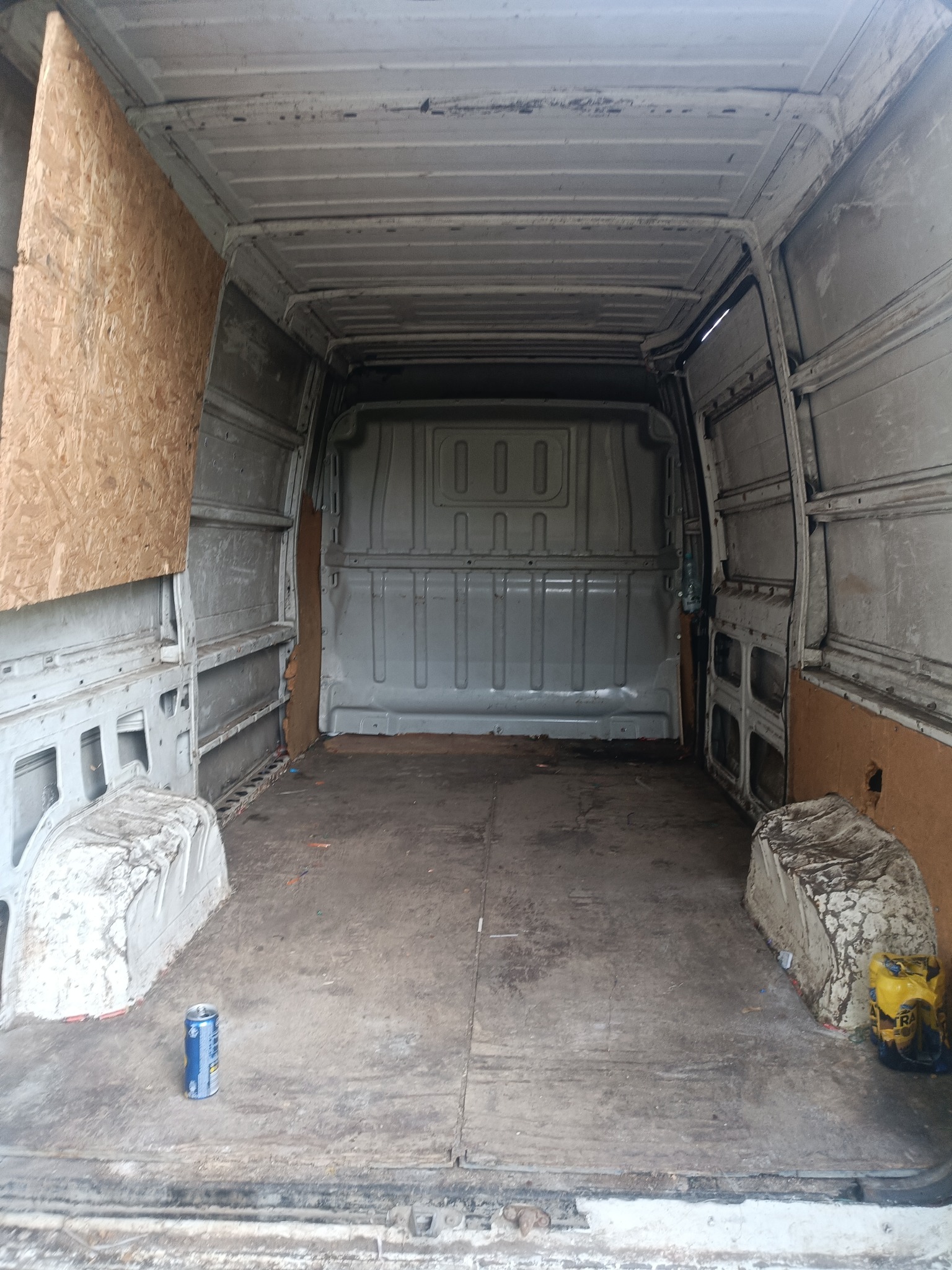 Wnętrze brudnego, częściowo wyłożonego sklejką busa. Na podłodze puszka i worek. Widok od tyłu pojazdu, drzwi otwarte.