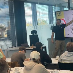 GEPARD SPÓŁKA Z OGRANICZONĄ ODPOWIEDZIALNOŚCIĄ - Szkolenie z obsługi wózków widłowych: instruktor prezentuje schemat na interaktywnej tablicy, uczestnicy siedzą przy stołach z notatkami i filiżankami.