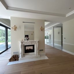 Ares Bud Hennadii Deleraikov - Eleganckie wnętrze z marmurowym kominkiem i drewnianą podłogą. Widoczne złote kinkiety i duże okno z widokiem na zieleń. Minimalistyczny design z dbałością o detale.