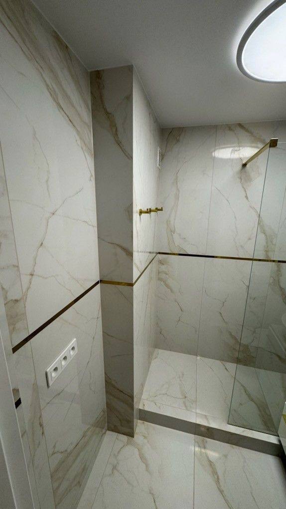 Elegancka kabina prysznicowa w Warszawie z marmurowymi płytkami i złotymi akcentami, widoczna listwa dekoracyjna i gniazdko elektryczne.