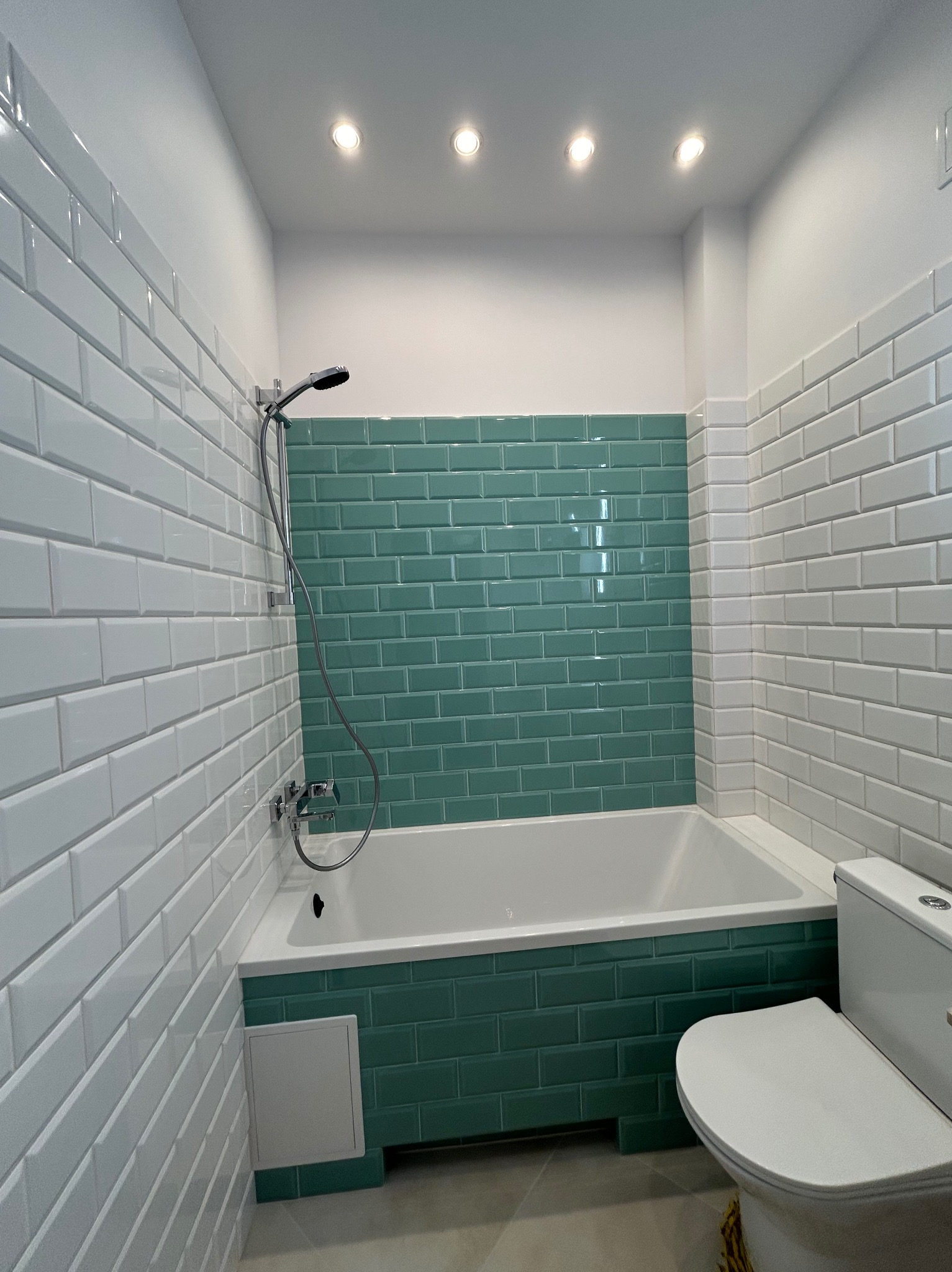 Biało-turkusowa łazienka z wanną obłożoną płytkami typu metro, widok z góry, oświetlenie punktowe, minimalistyczny styl.