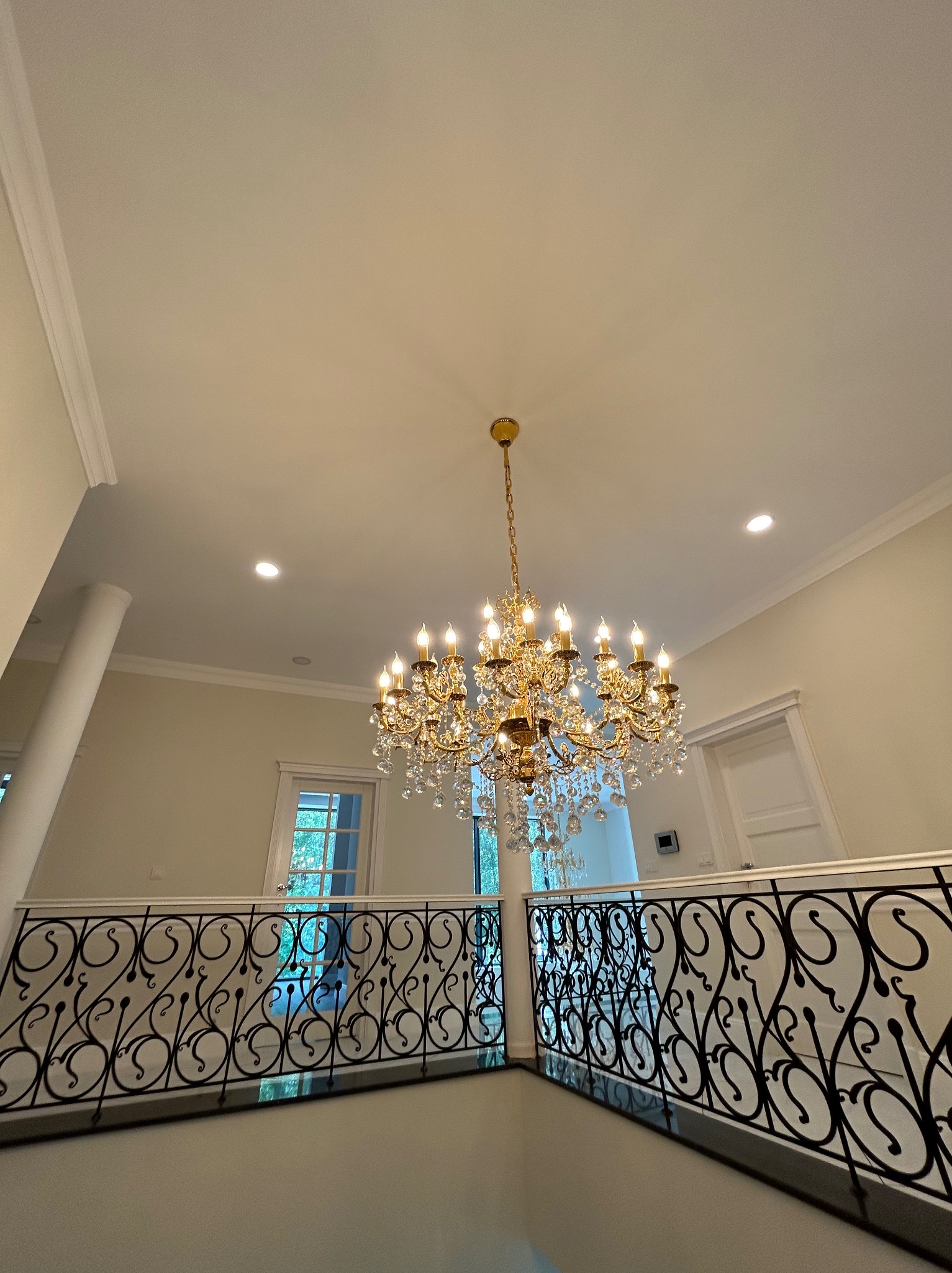 Elegancki, wysoki hol z kryształowym żyrandolem i ozdobną, kutą balustradą. Widoczne detale wykończenia ścian i sufitu, podkreślające luksusowy charakter wnętrza.