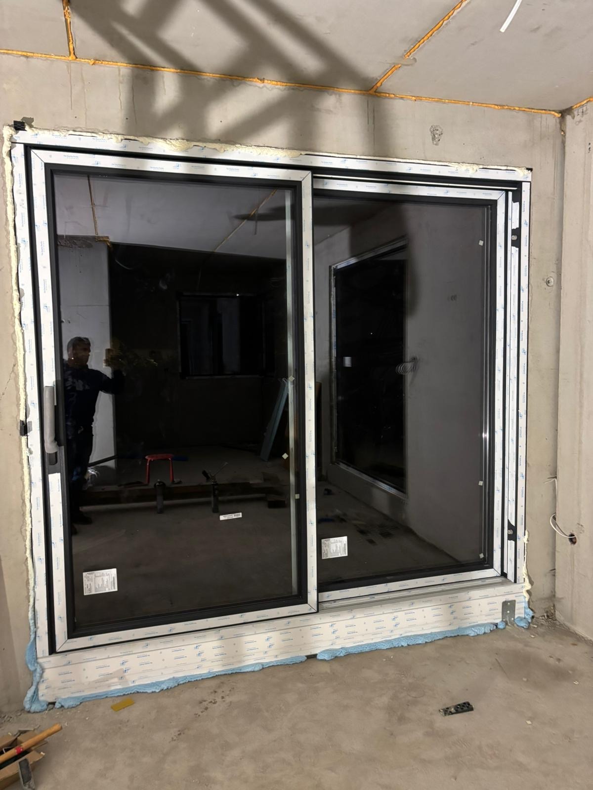 Zamontowane, czarne drzwi przesuwne z białymi ramami, widoczne pianka montażowa i surowy beton. W tle widoczny pracownik i wnętrze w trakcie wykończenia.