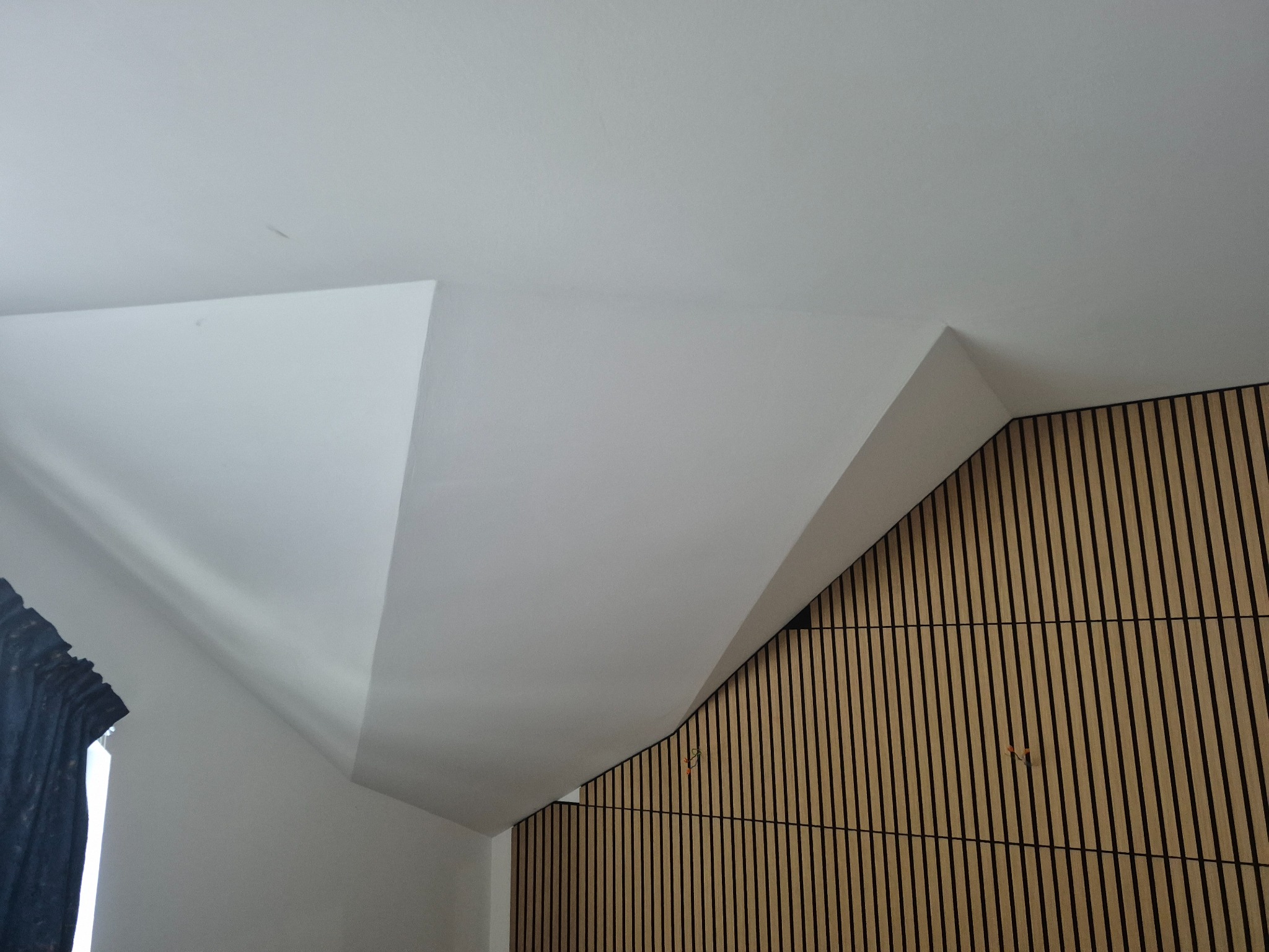 Wykończone poddasze z nietypowym łączeniem sufitu i ściany z drewnianymi panelami. Biały sufit z płyt gipsowych, skośny. Widoczne mocowania paneli.