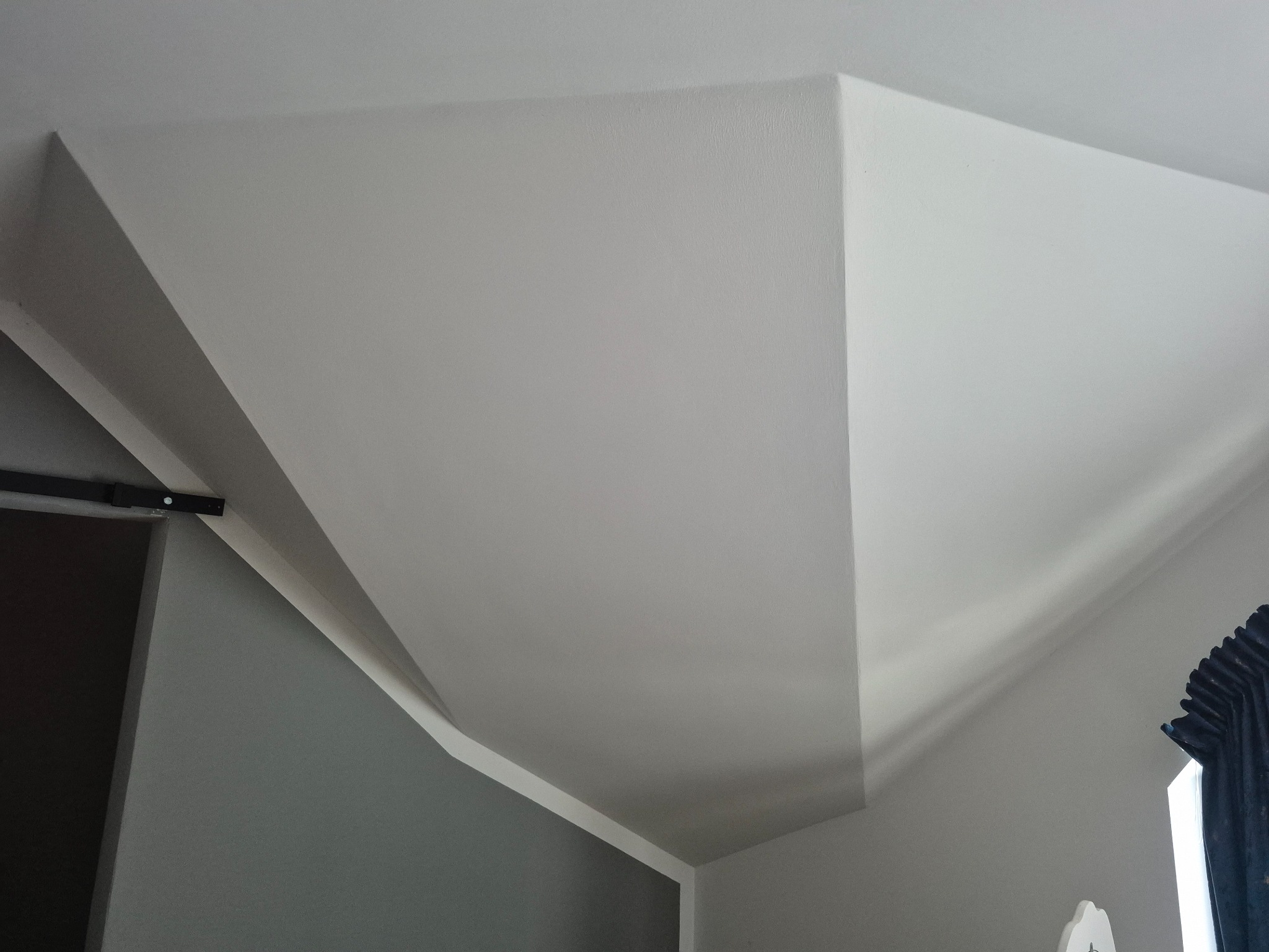 Wykończone poddasze z płyt w Dobre Miasto: skosy sufitowe i ściany pomalowane na biało, widoczne detale wykończeniowe i fragment zasłony.