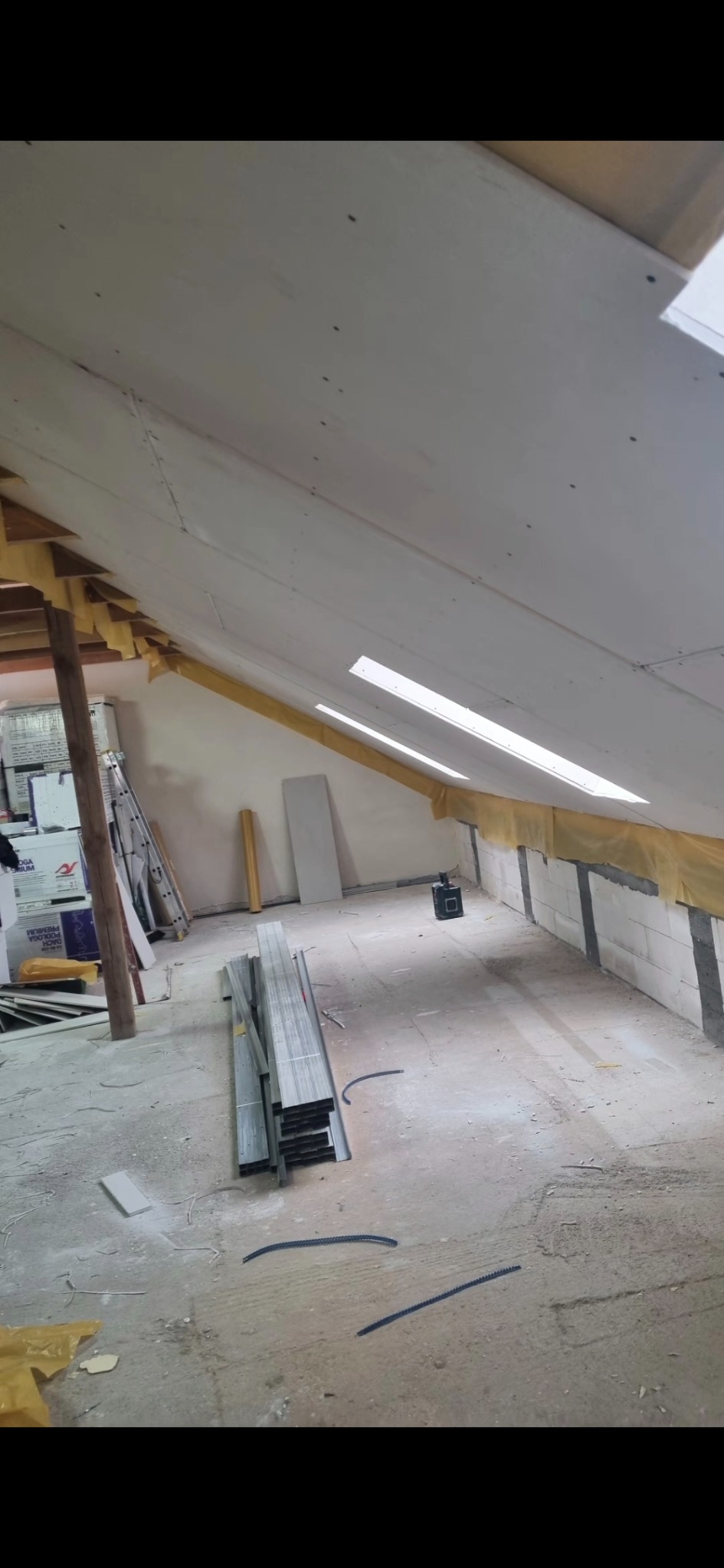 Montaż płyt na poddaszu z oknami dachowymi. Widoczne profile, izolacja i narzędzia. Prace wykończeniowe w trakcie realizacji. Ujęcie z dołu, surowe wnętrze.