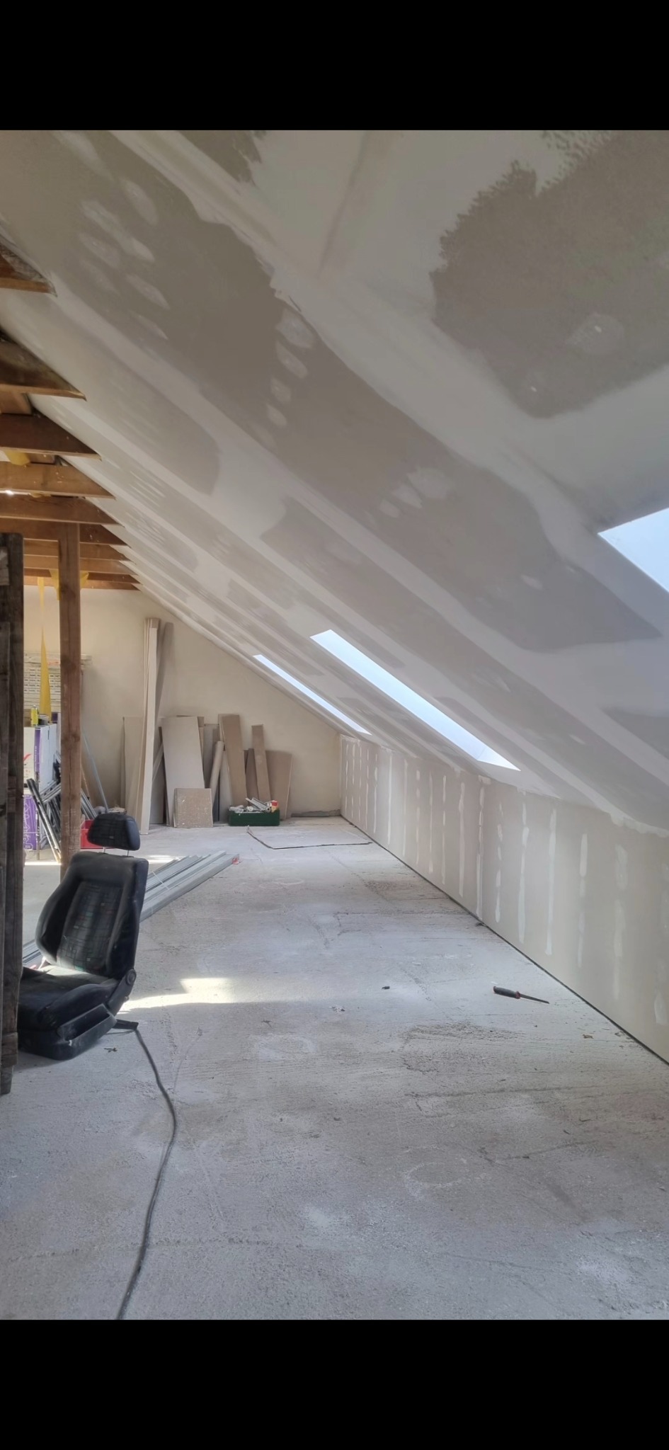 Montaż płyt na poddaszu z oknami dachowymi. Widoczne drewniane elementy konstrukcyjne i przygotowane płyty. Prace wykończeniowe w trakcie realizacji.