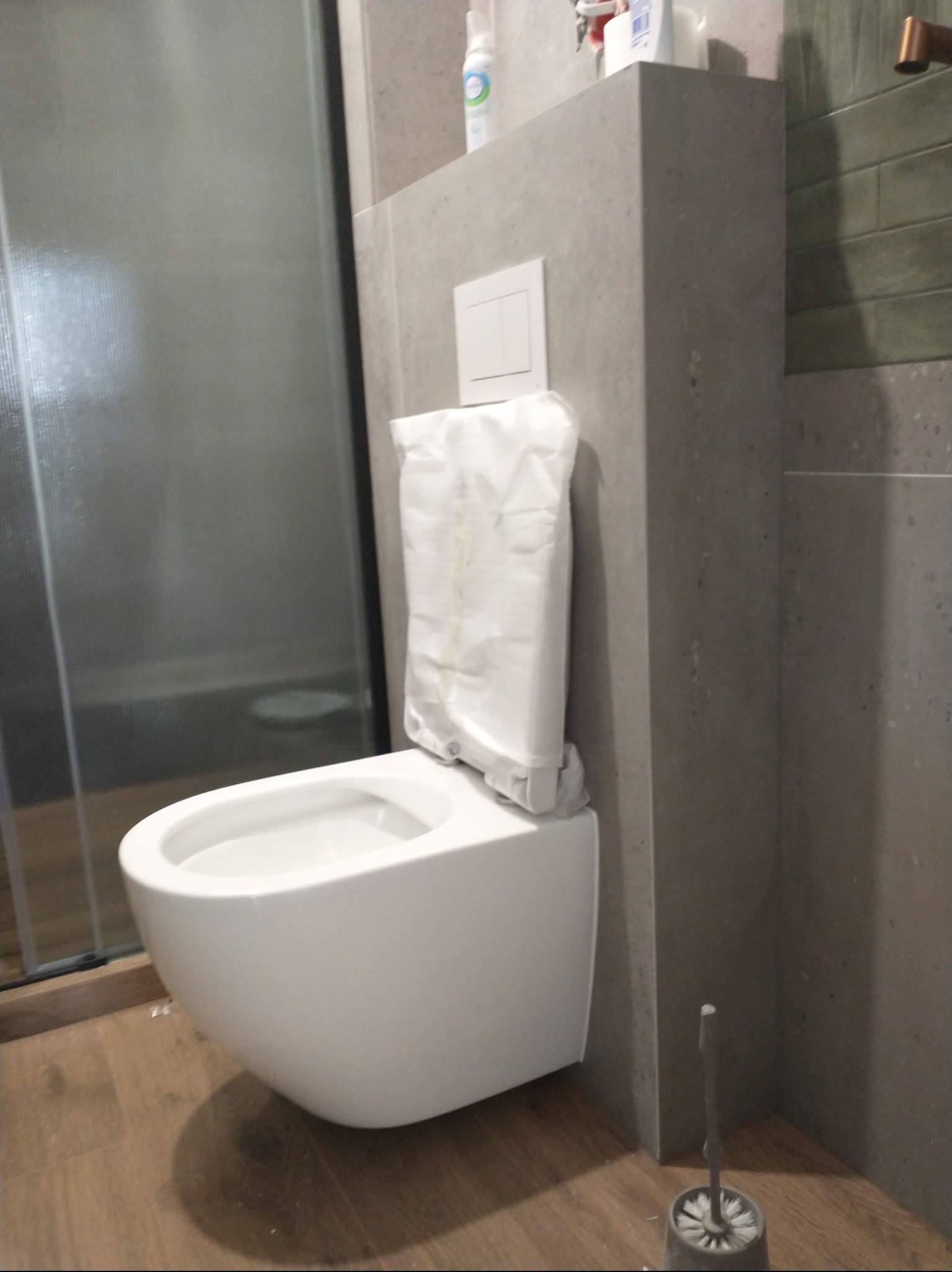 Nowoczesna, podwieszana toaleta w łazience z szarą zabudową i drewnopodobną podłogą. Widoczna kabina prysznicowa i akcesoria łazienkowe.