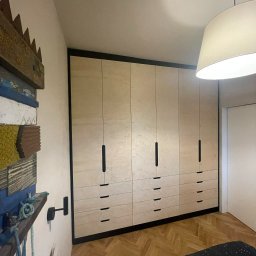 NEUROOM Katarzyna Nojman - Jasna, drewniana szafa wnękowa z czarnymi detalami w sypialni z parkietem i dekoracjami ściennymi. Minimalistyczny design, ciepłe oświetlenie.
