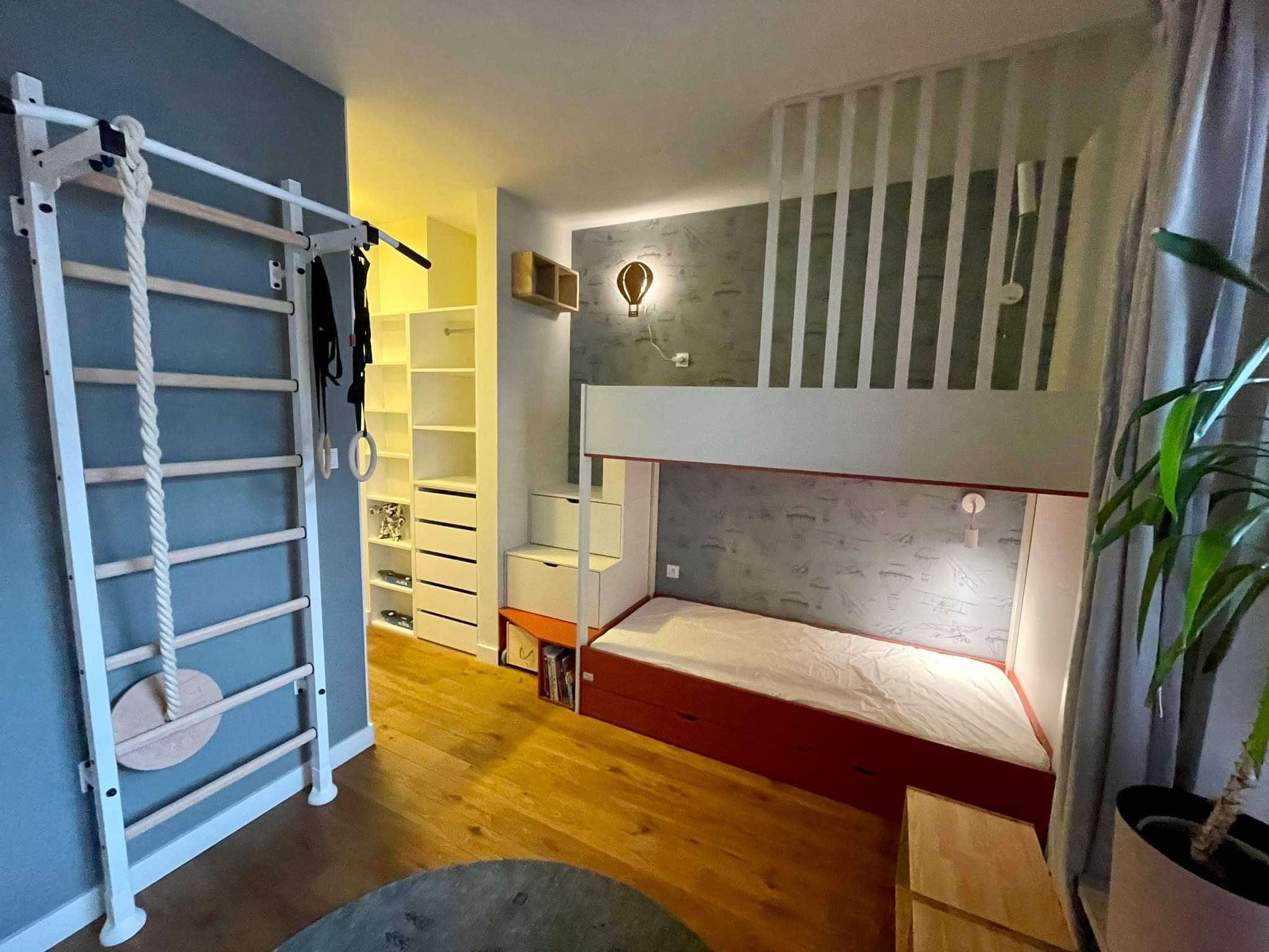 Pokój dziecięcy z łóżkiem piętrowym, drabinką gimnastyczną i szafą wnękową. Oświetlenie w kształcie balonu. Parkiet na podłodze. Nowoczesny wystrój.