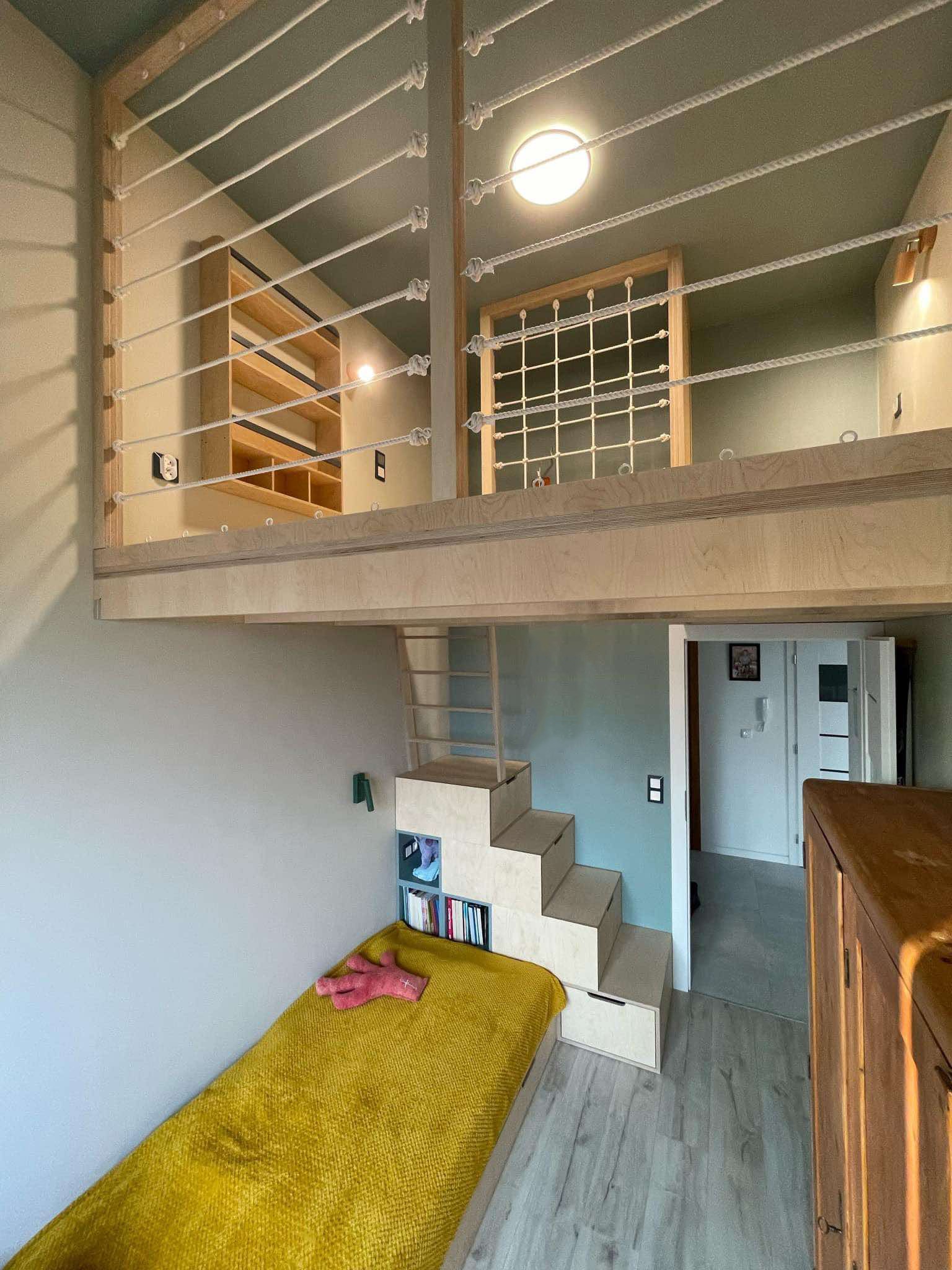 Pokój dziecięcy z antresolą i schodami z szufladami. Żółte łóżko, drewniane wykończenia, liny jako balustrada. Nowoczesny design, jasne kolory, funkcjonalne rozwiązania.