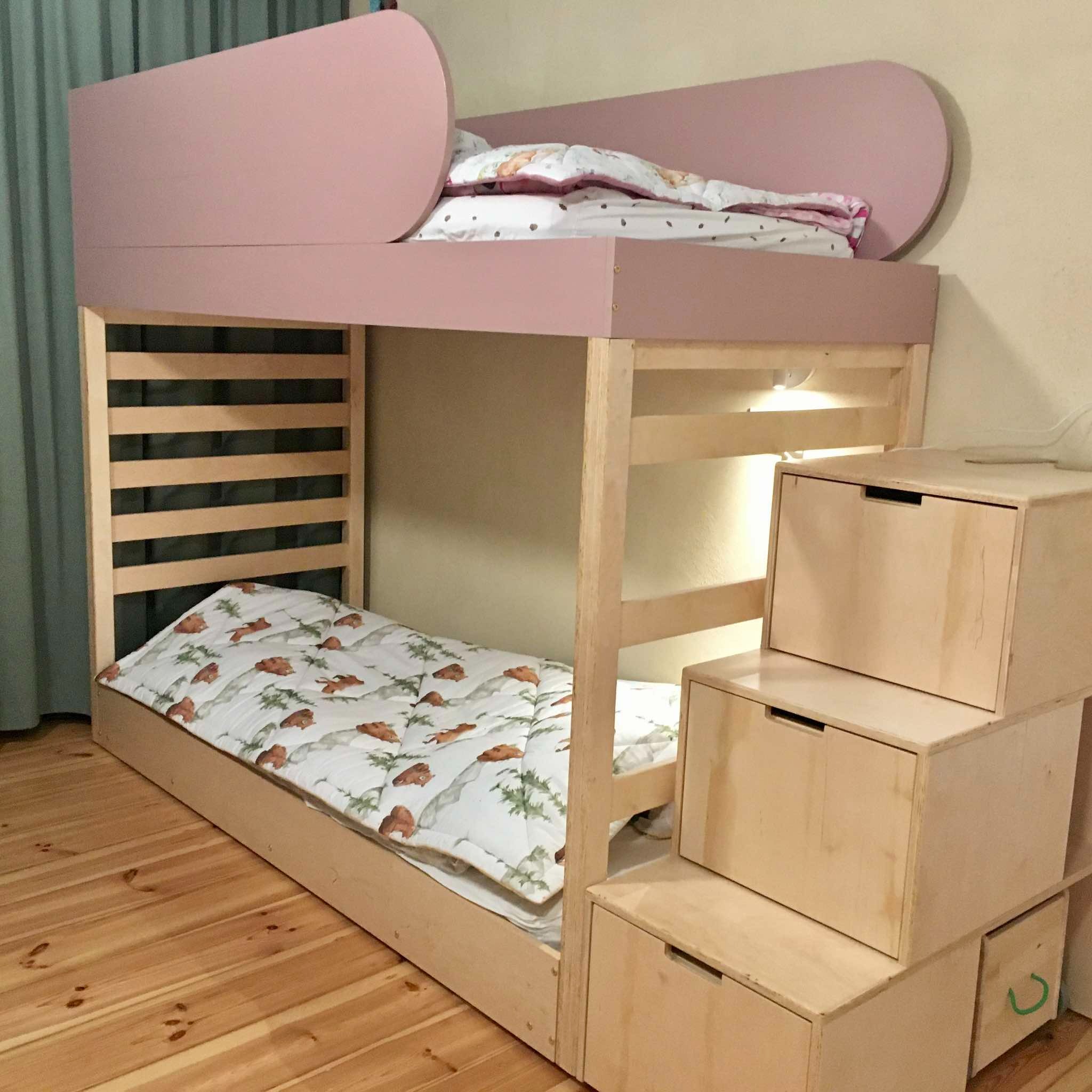 Drewniane łóżko piętrowe z różowym wykończeniem i schodami z szufladami, oświetlone od spodu, na drewnianej podłodze. Widok z bliska na detale konstrukcji.