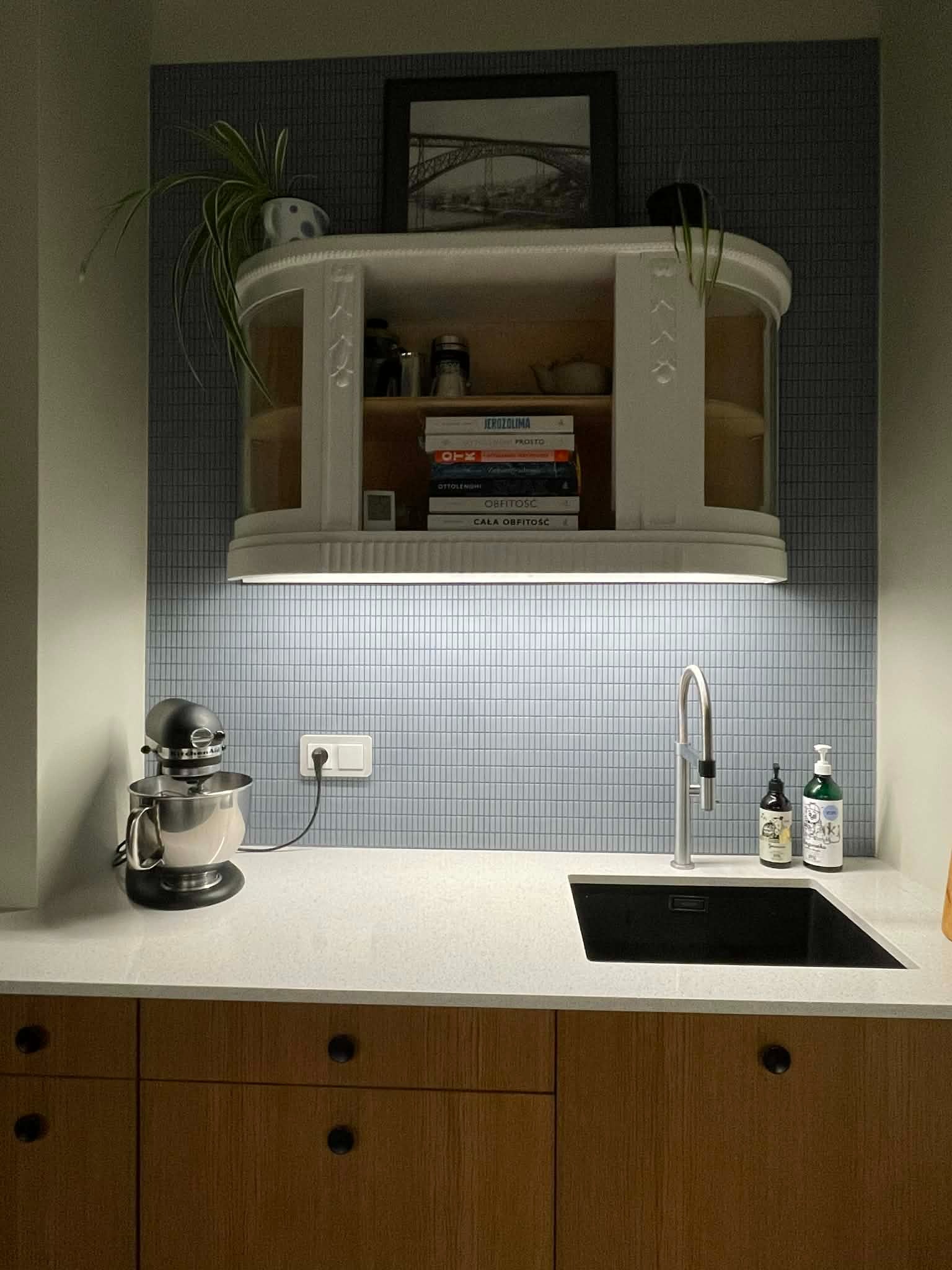 Kuchenna aranżacja w Wejherowie: biała szafka wisząca nad blatem z czarnym zlewem, mozaika na ścianie i mikser stojący. Nowoczesny design z elementami retro.