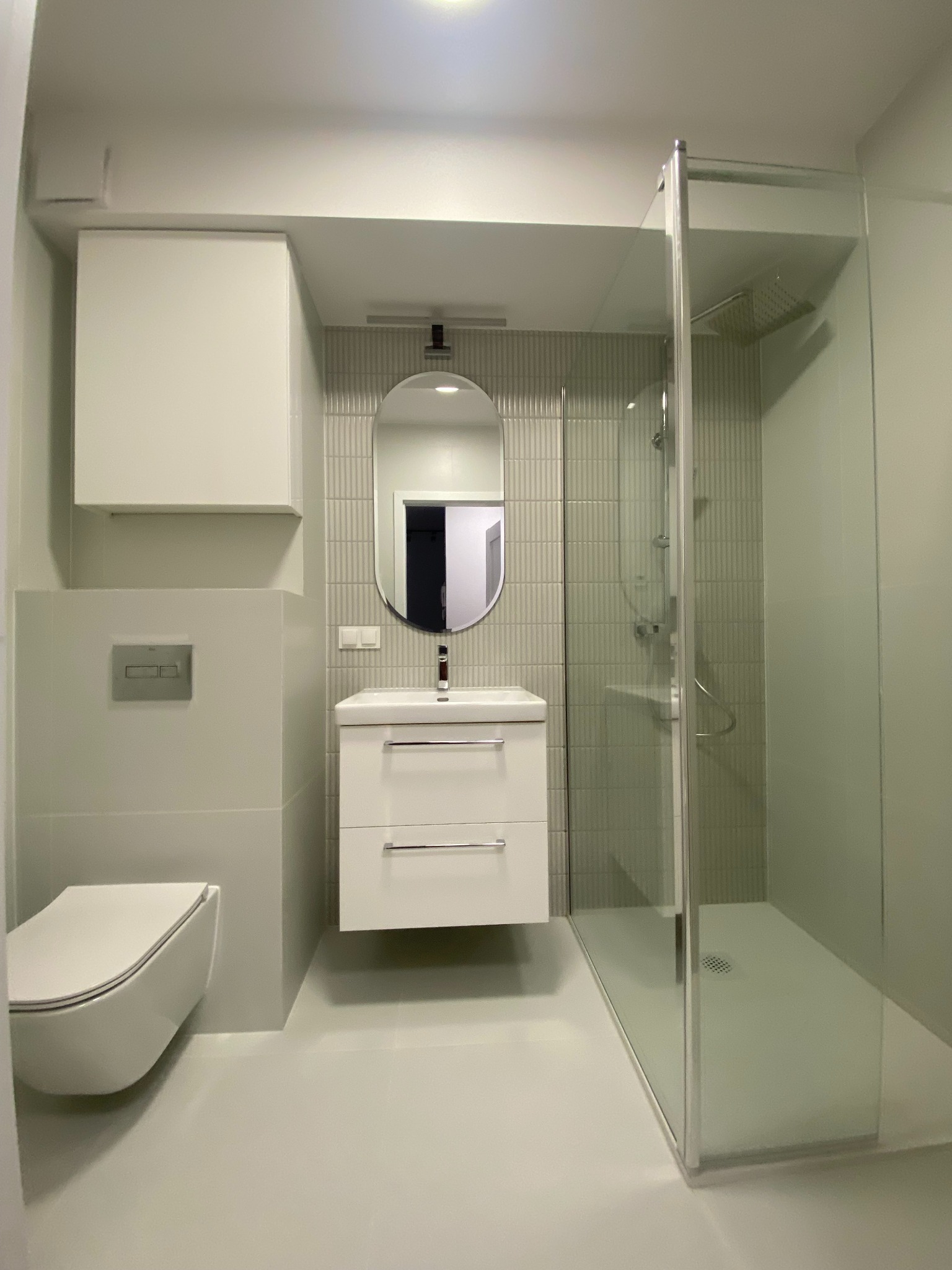 Nowoczesna łazienka w odcieniach bieli i szarości. Kabina prysznicowa ze szklanymi ścianami, podwieszana toaleta i umywalka z szafką. Minimalistyczny design.