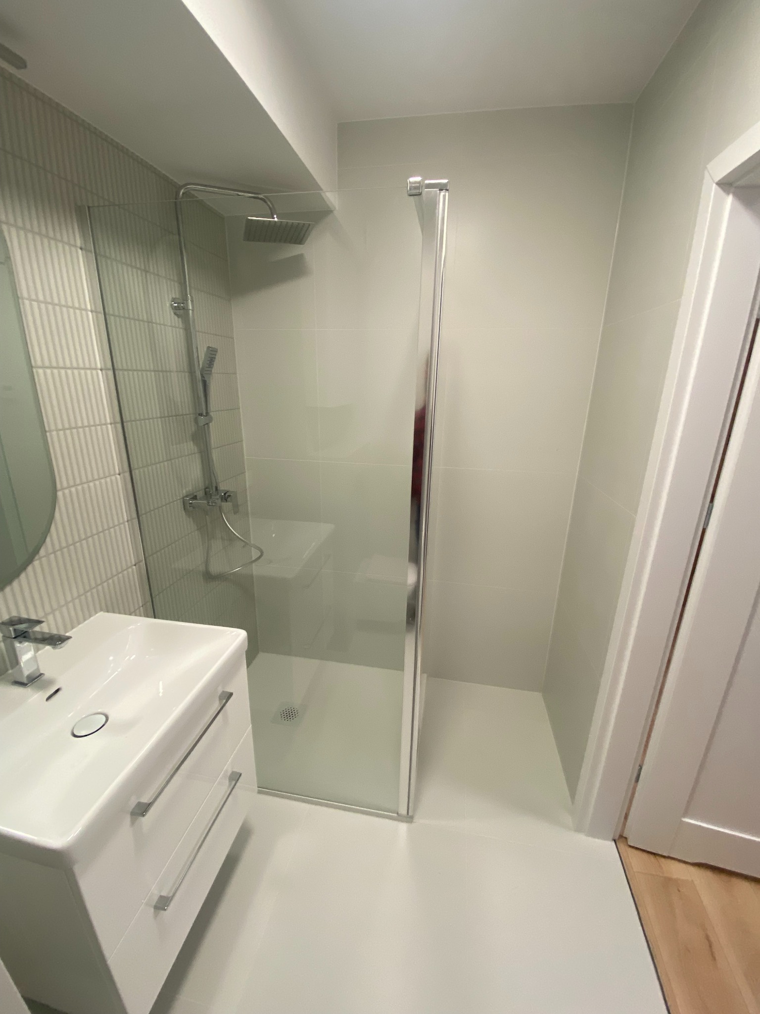 Jasna łazienka po remoncie: biała umywalka z szafką, kabina prysznicowa ze szklanymi drzwiami, płytki w odcieniach bieli i szarości. Minimalistyczny design.