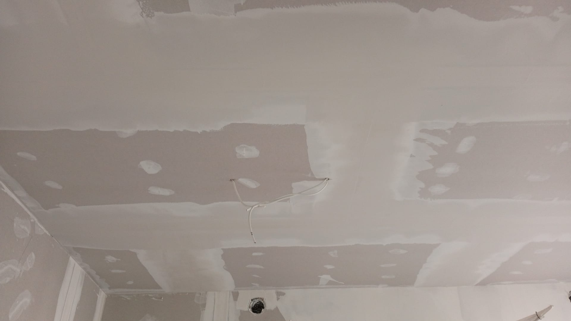 Nierównomiernie wyszpachlowany sufit z widocznymi przewodami elektrycznymi i otworami, przygotowany do dalszych prac wykończeniowych. Szpachlowanie w trakcie realizacji.