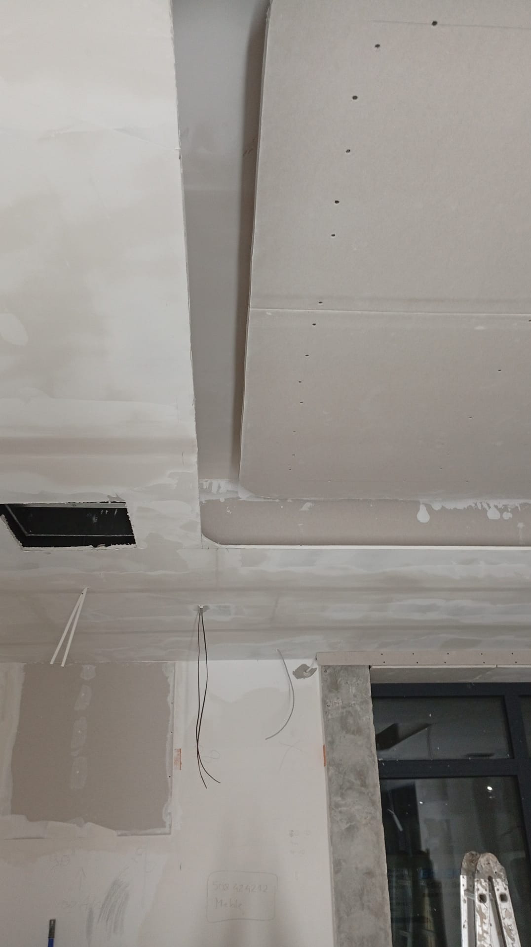 Sufit podwieszany z płyt karton-gips, widoczne łączenia i otwór na oświetlenie. Na ścianie widoczne ślady po pracach wykończeniowych i wystające przewody.