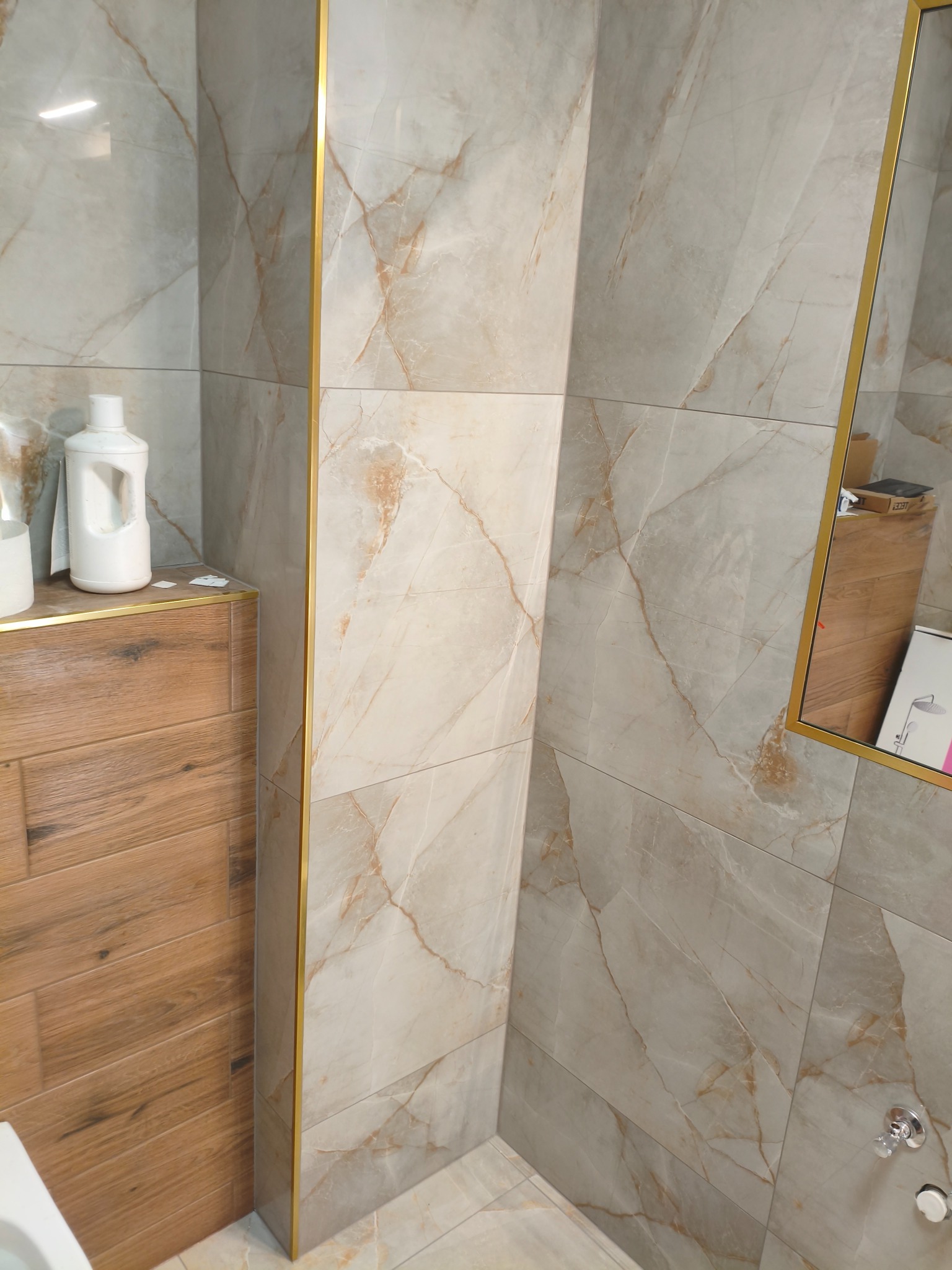 Wykończona łazienka z marmurowymi płytkami w odcieniach beżu i brązu, z akcentami w kolorze złota. Widoczna umywalka i lustro.