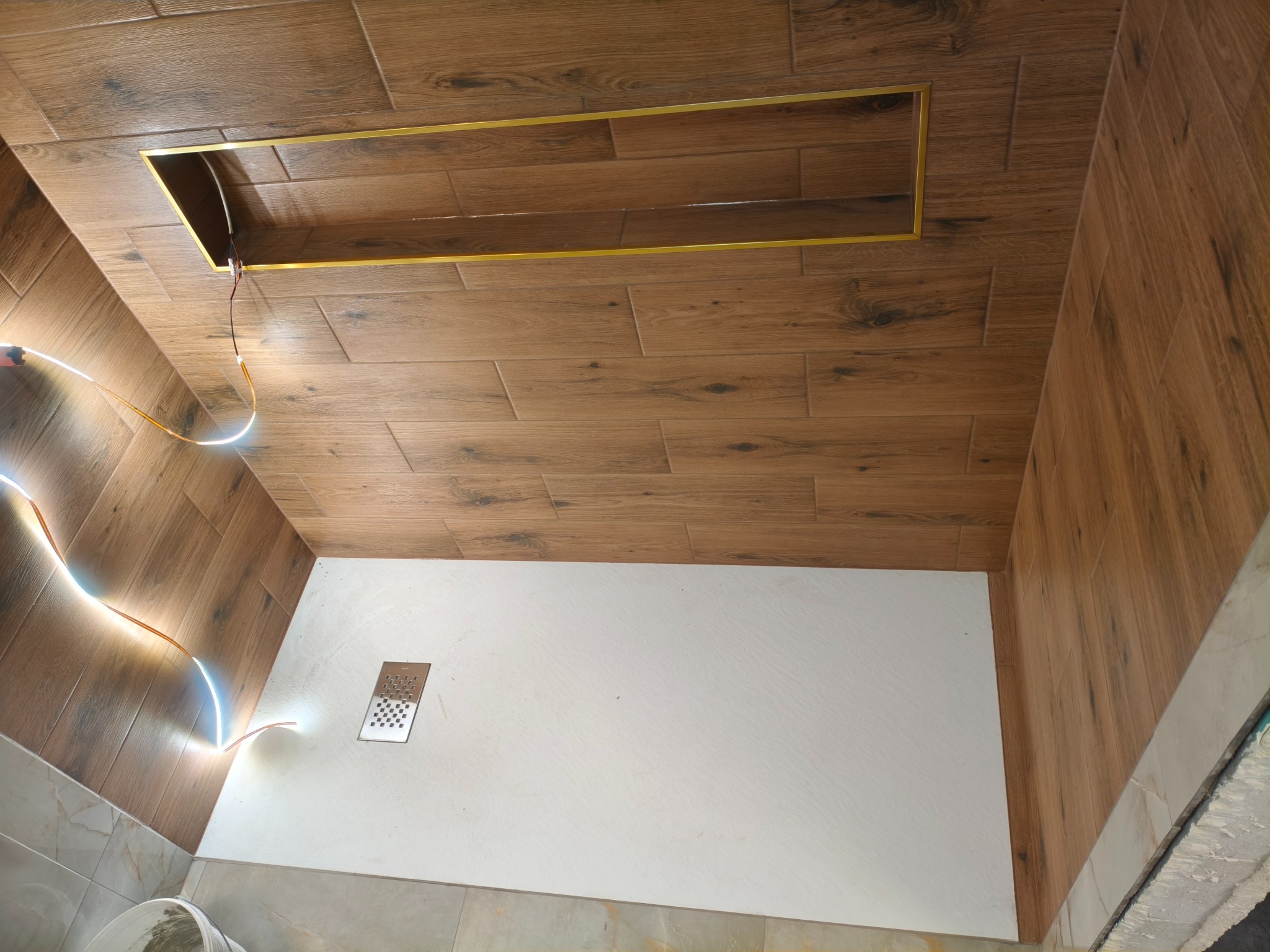 Wykończona kabina prysznicowa z drewnopodobnymi płytkami na ścianach i suficie, oświetleniem LED i odpływem liniowym. Widok z góry.