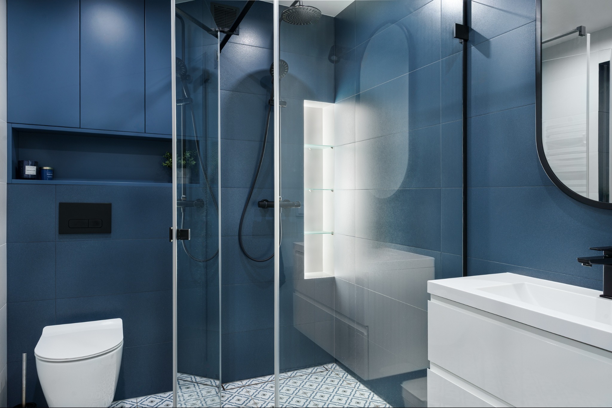 Niebieska łazienka z kabiną prysznicową i wzorzystą podłogą w Kwaśniowie Dolnym. Nowoczesne oświetlenie i czarne akcenty tworzą elegancki wystrój.