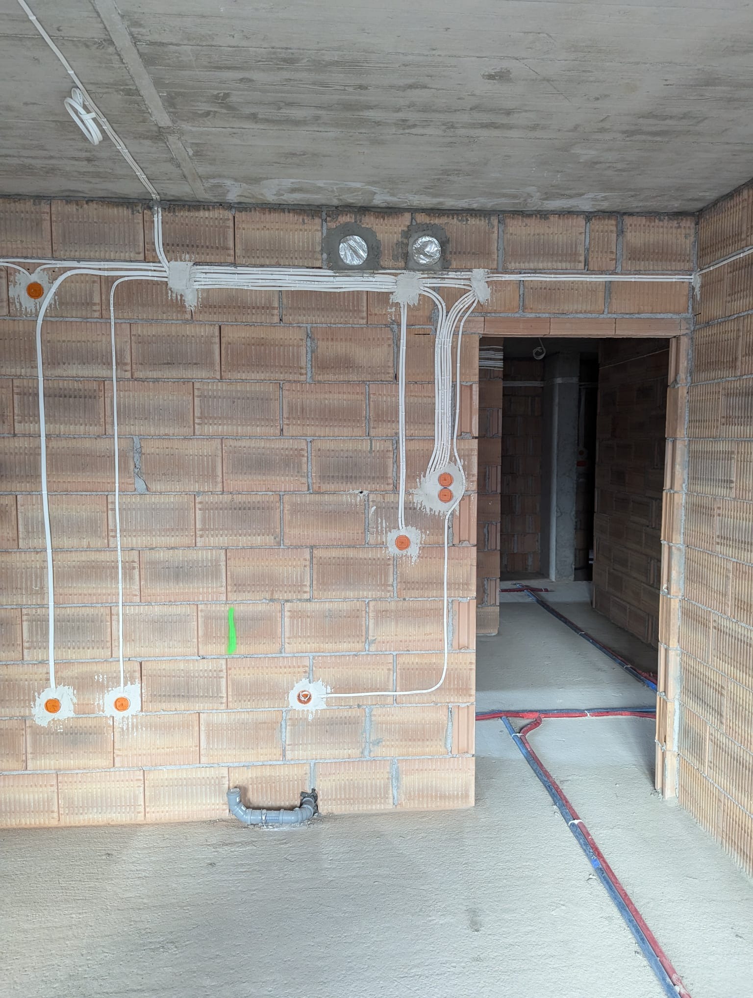 Instalacja elektryczna w surowym wnętrzu z cegły dziurawki w Rudniku. Widoczne kable, puszki i rury. Instalacja prowadzona natynkowo, sufit betonowy.