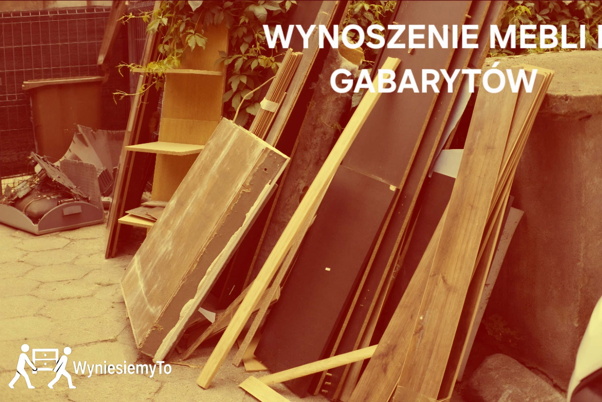 Stos mebli i gabarytów przygotowanych do wywiezienia, opartych o betonowy murek i ogrodzenie. Widoczne elementy szafek, deski i inne odpady. Ujęcie z dołu.