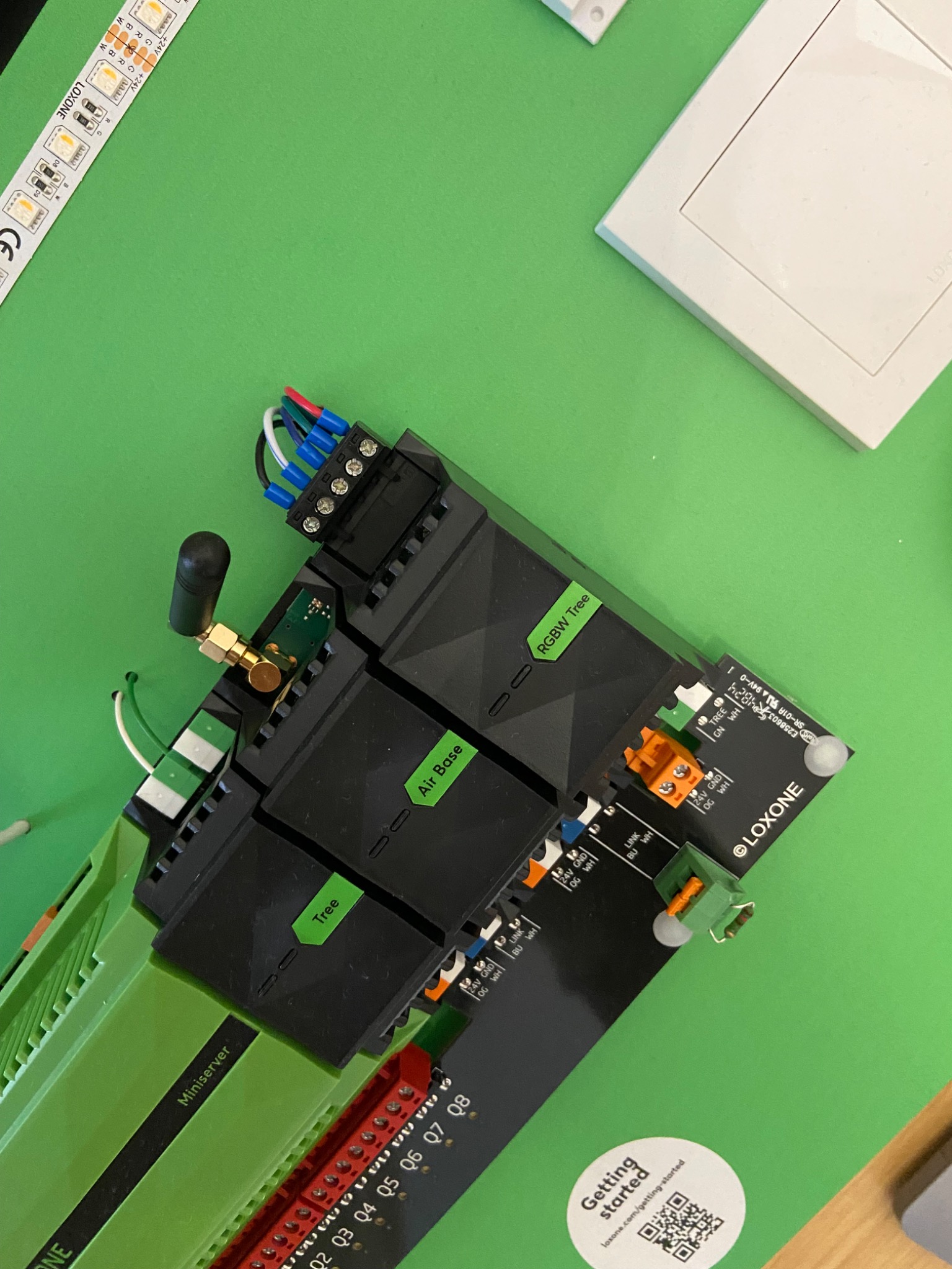Panel sterowania inteligentnego domu Loxone z podłączonymi przewodami, widoczne moduły Air Base, RGBW Tree i Miniserver na zielonym tle.