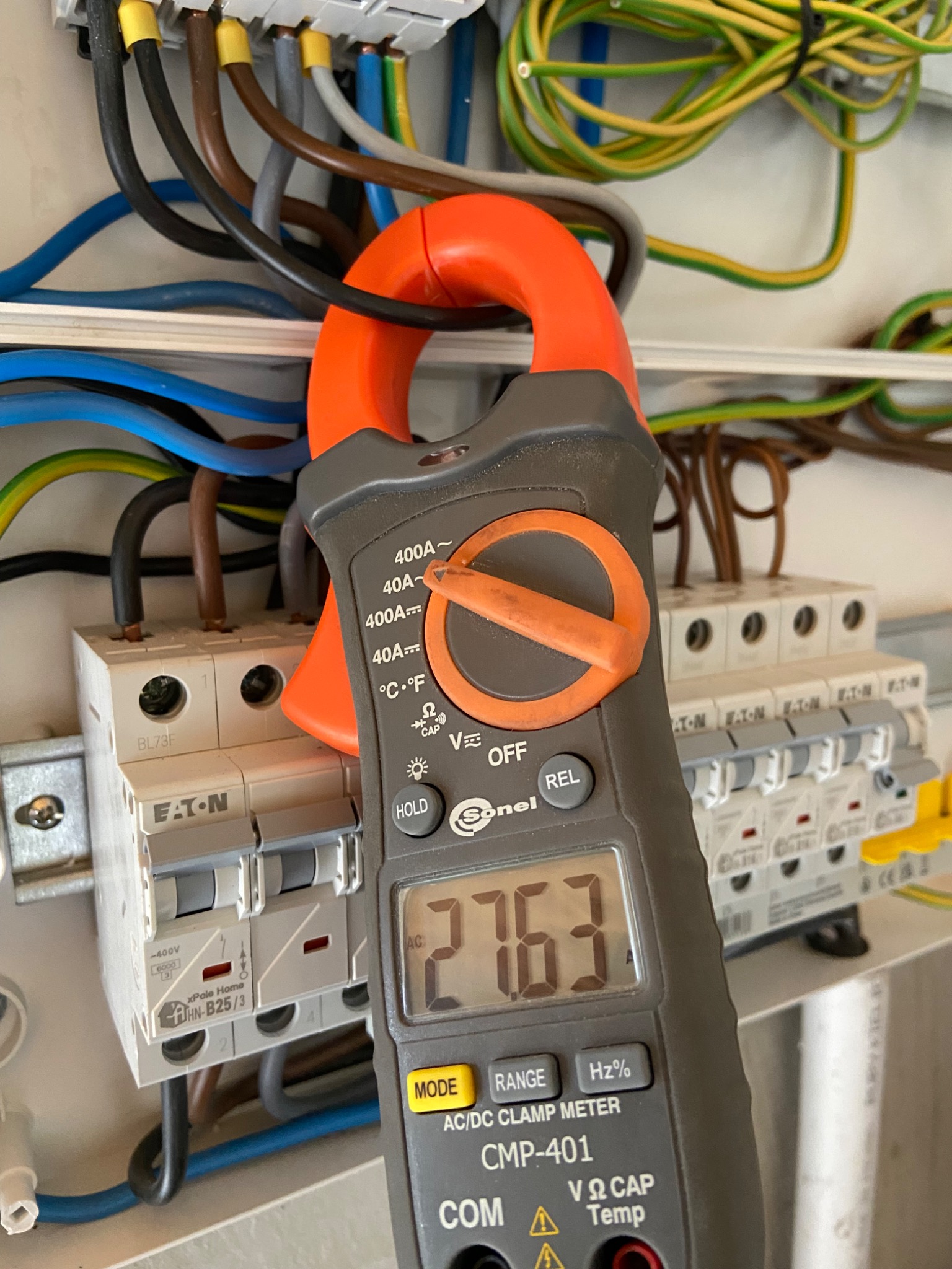 Pomiar prądu w rozdzielnicy elektrycznej za pomocą miernika cęgowego Sonel CMP-401. Widoczne kable, bezpieczniki Eaton i wynik pomiaru 2763.