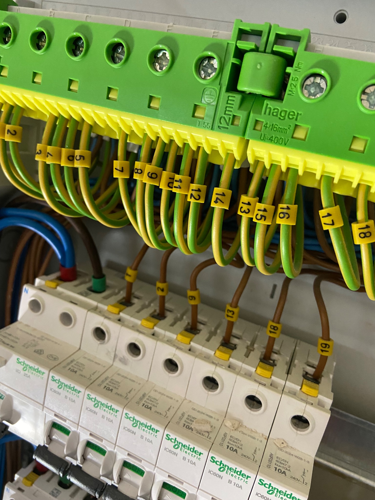 Szczegółowe ujęcie rozdzielnicy elektrycznej z numerowanymi przewodami, bezpiecznikami Schneider Electric i elementami Hager, ukazujące profesjonalny montaż.