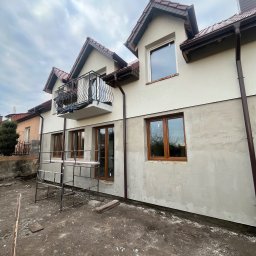 Bohdan Onyshchuk - Dom z balkonem w trakcie prac elewacyjnych: górna część pomalowana na kremowo, dolna w szarym tynku. Widoczne rusztowania i brązowe rynny.