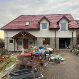 Bohdan Onyshchuk - Dom w trakcie tynkowania elewacji w Goleniowie. Widoczne przygotowane materiały budowlane i częściowo otynkowana fasada. Czerwona dachówka i drewniane elementy.