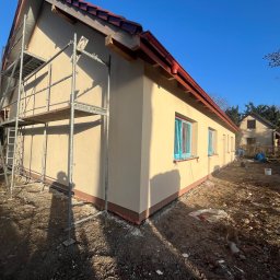 Bohdan Onyshchuk - Budynek po tynkowaniu z rusztowaniem. Okna zabezpieczone folią. Widoczne detale wykończenia i przygotowania do dalszych prac elewacyjnych w słoneczny dzień.