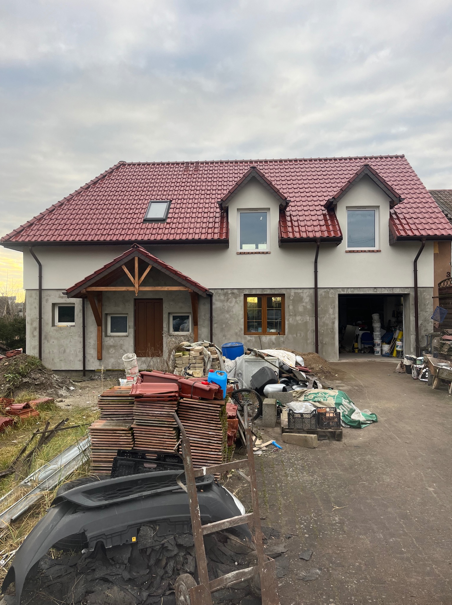 Dom w trakcie tynkowania elewacji w Goleniowie. Widoczne przygotowane materiały budowlane i częściowo otynkowana fasada. Czerwona dachówka i drewniane elementy.