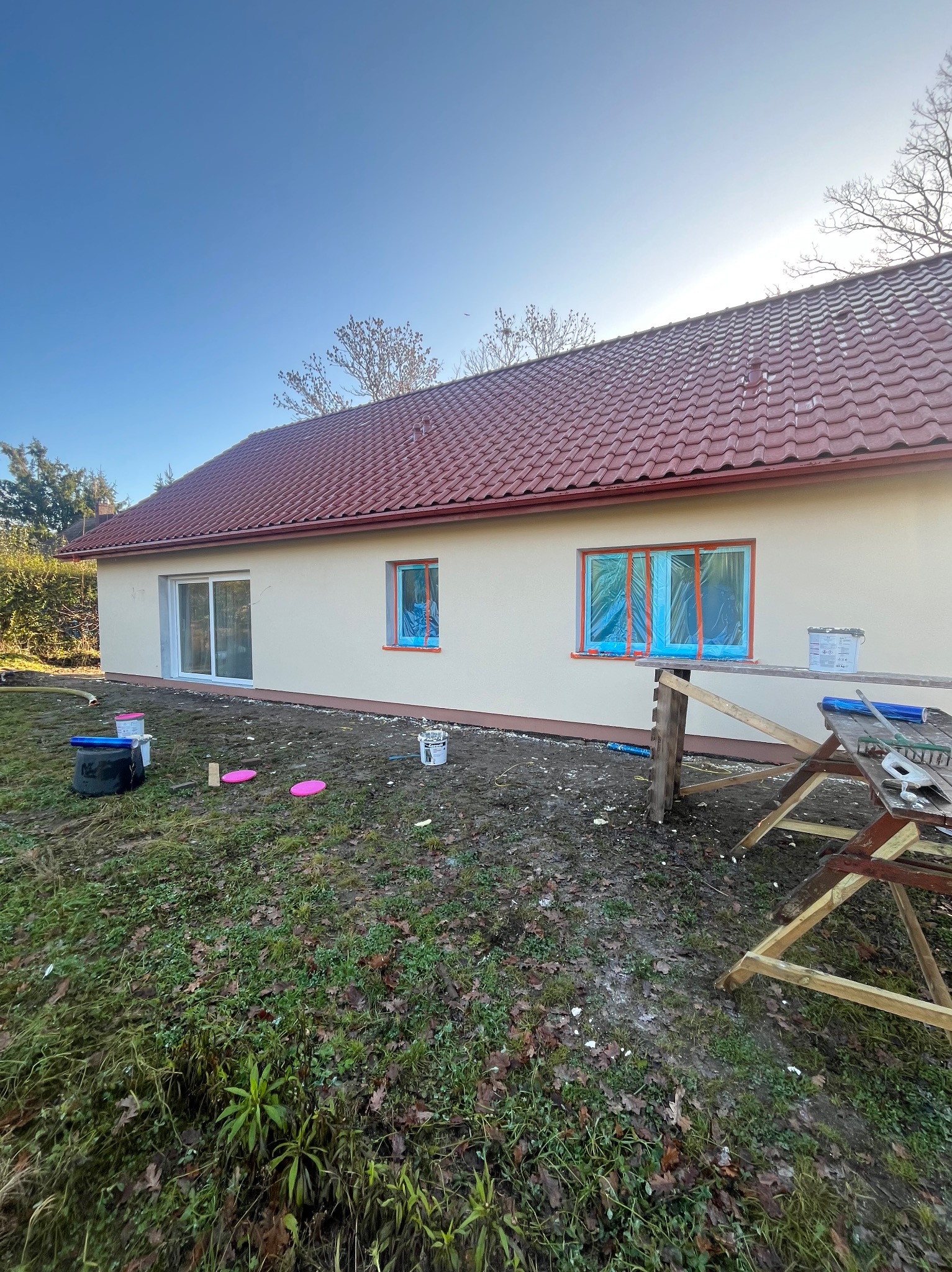Dom jednorodzinny po tynkowaniu, z oknami zabezpieczonymi folią i rozstawionym rusztowaniem. Świeżo nałożony tynk w kolorze kremowym.