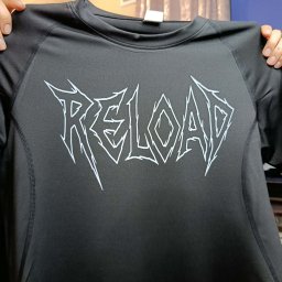 Aleksandra Rusin ZRYW WEAR - Czarna koszulka sportowa z białym, stylizowanym napisem 'RELOAD' prezentowana z bliska, trzymana przez osobę. Widoczne szwy i detale materiału.