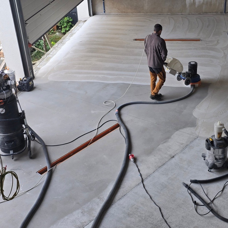 Przygotowanie betonowej posadzki w hali serwisowej pod żywicę. Szlifowanie maszyną, odkurzacze przemysłowe, widoczny pracownik w trakcie pracy.