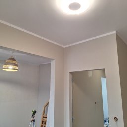 Kamil Stępiński - Wnętrze po malowaniu ścian na beżowo z białym wykończeniem sufitu. Widoczny laser krzyżowy, lampa wisząca i fragment drabiny.