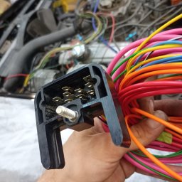Kudłaty - Złącze elektryczne z kolorowymi przewodami w dłoni, widoczne elementy silnika samochodowego w tle. Detal naprawy instalacji elektrycznej pojazdu.