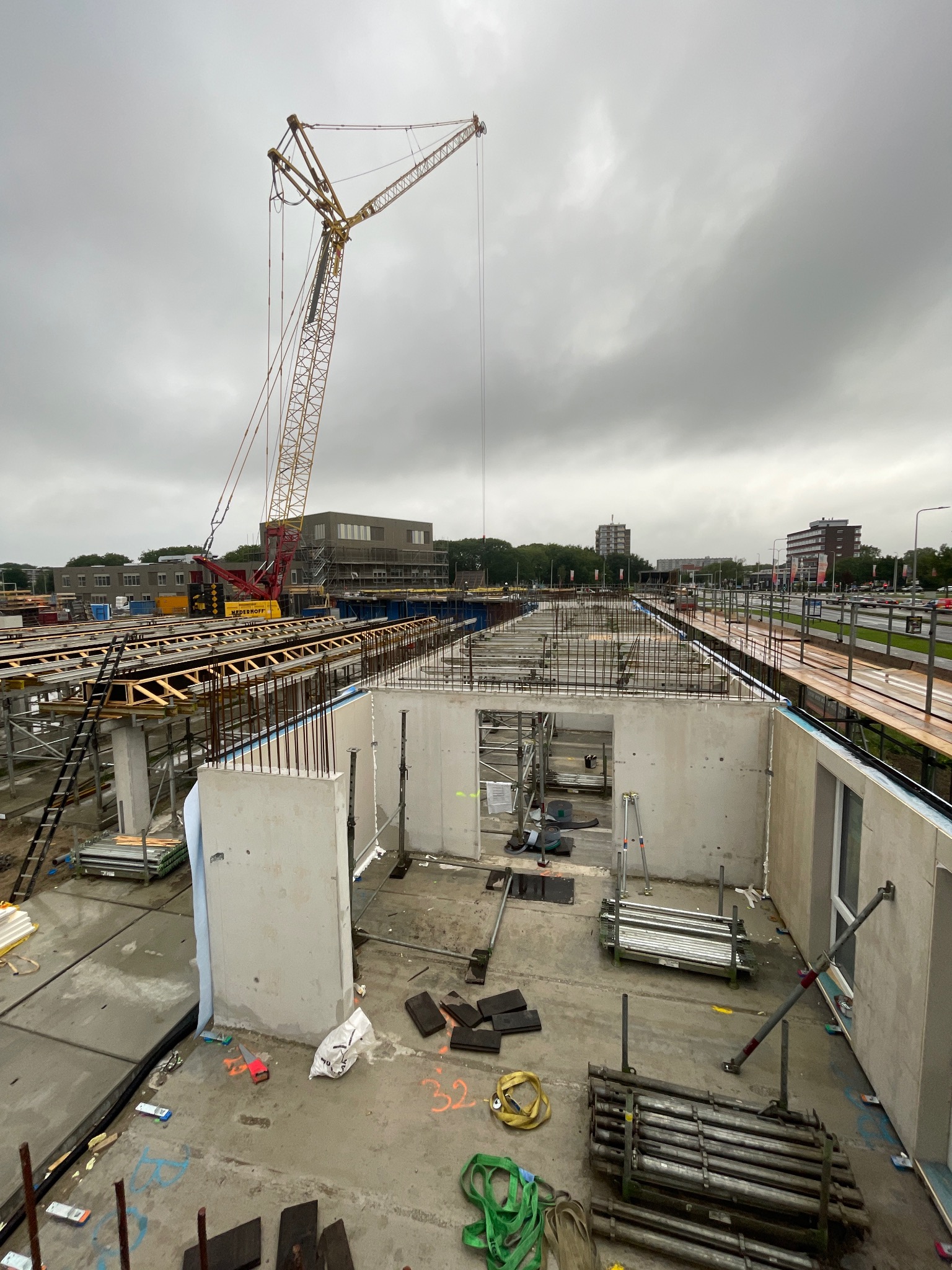 Budowa budynku z betonu: widok z góry na szkielet konstrukcji, zbrojenia i dźwig na tle pochmurnego nieba. Elementy szalunków i rusztowań widoczne w kadrze.