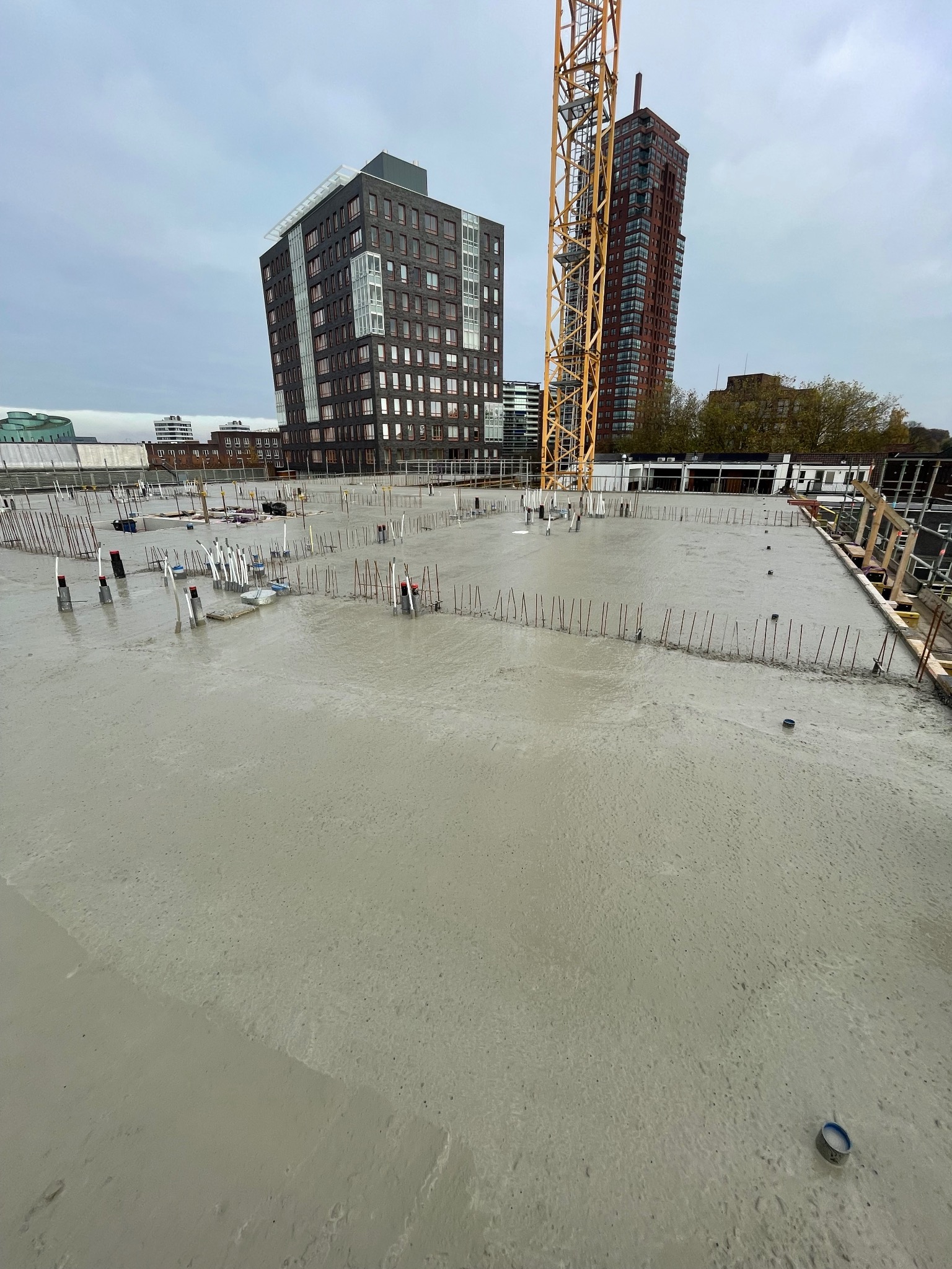 Zalany beton na stropie budynku w Białymstoku. Widoczne wystające pręty zbrojeniowe i elementy instalacji. W tle budynki mieszkalne i żuraw budowlany.