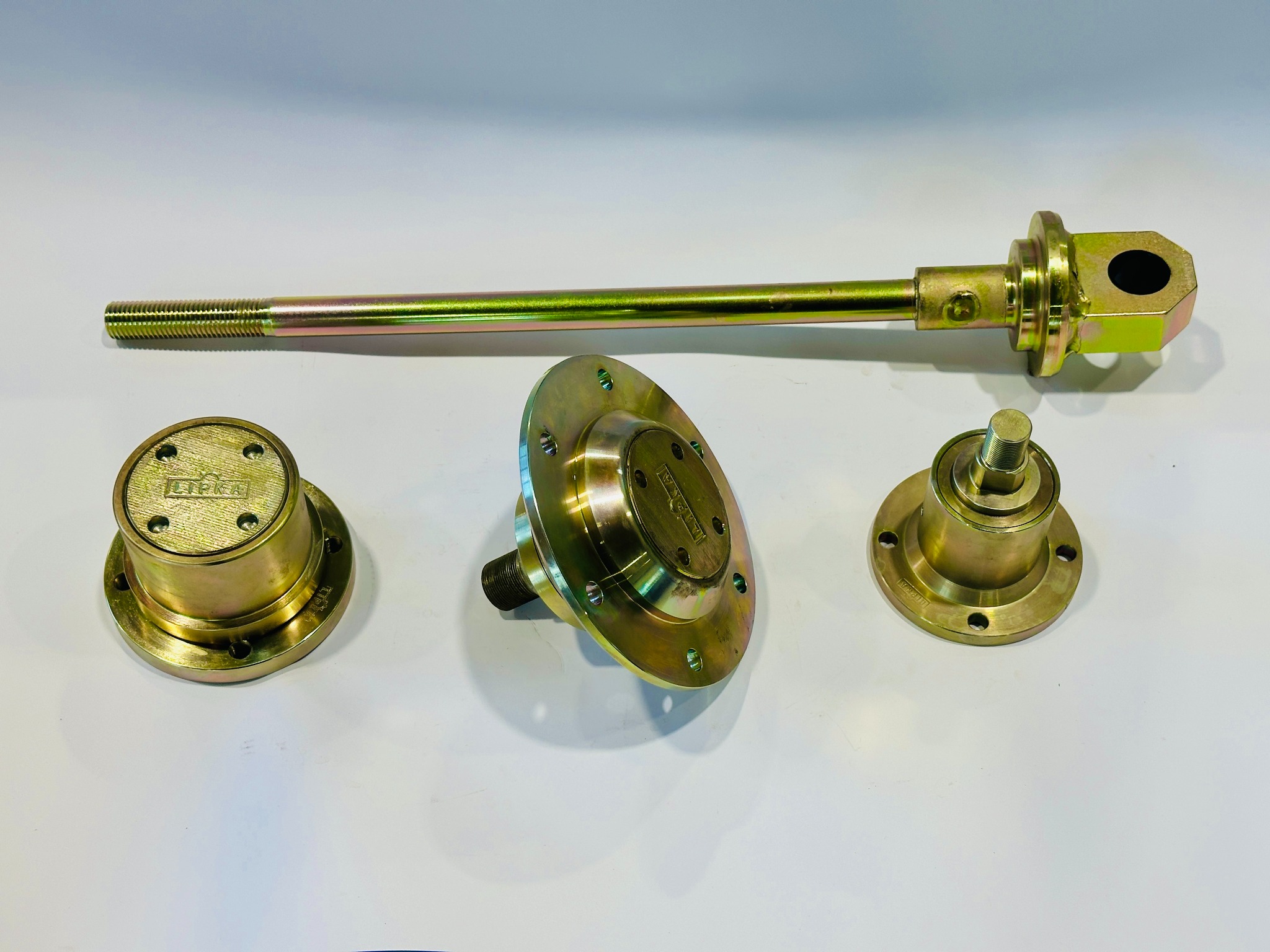 Precyzyjnie wykonane, metalowe elementy z gwintem i kołnierzami, pokryte złotą powłoką, ułożone na białym tle. Widoczne detale obróbki i mocowania.