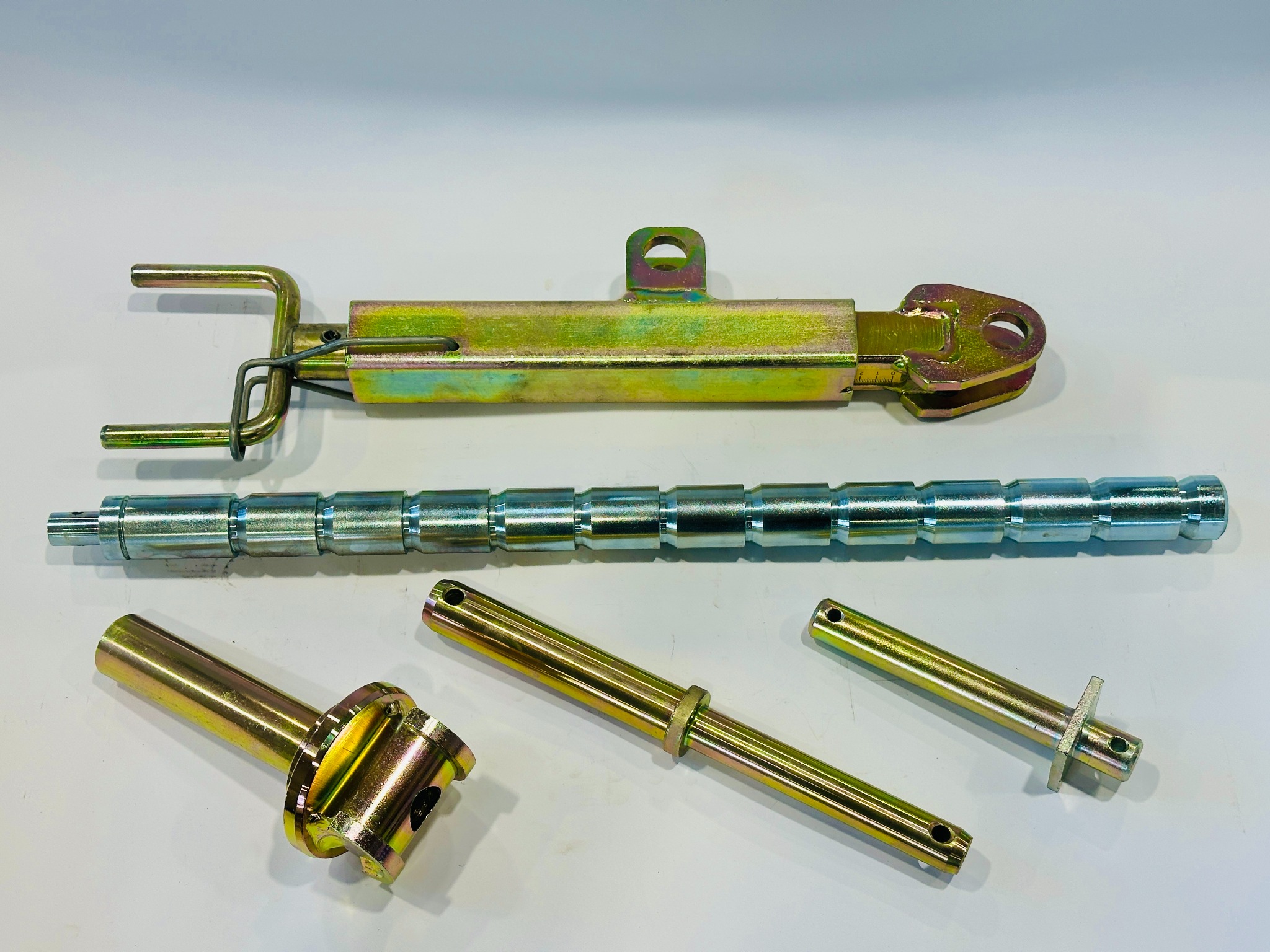 Precyzyjnie wykonane, metalowe elementy maszyn rolniczych w odcieniach złota i srebra, ułożone na białym tle. Widoczne detale obróbki i wykończenia.