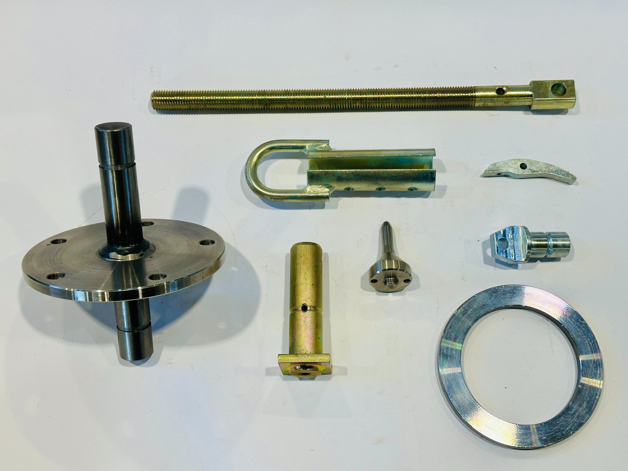 Zestaw precyzyjnie wykonanych, metalowych elementów: tuleja z kołnierzem, gwintowany pręt, uchwyt, pierścień i inne detale, prezentujących obróbkę metali.