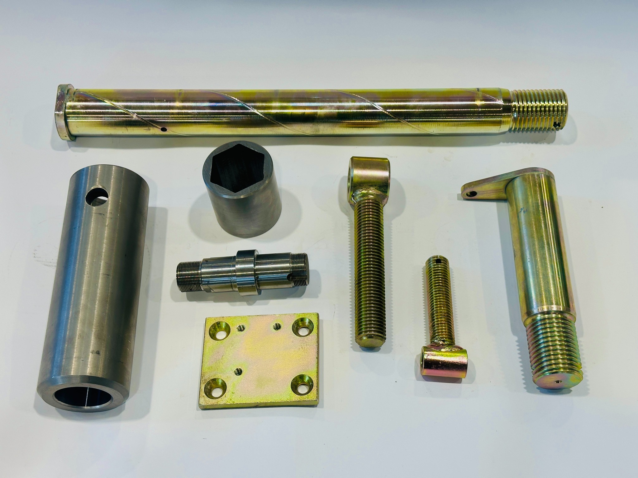 Precyzyjnie wykonane, metalowe elementy z gwintami i otworami, pokryte złotą powłoką, ułożone na białym tle. Widoczne detale obróbki i wykończenia.