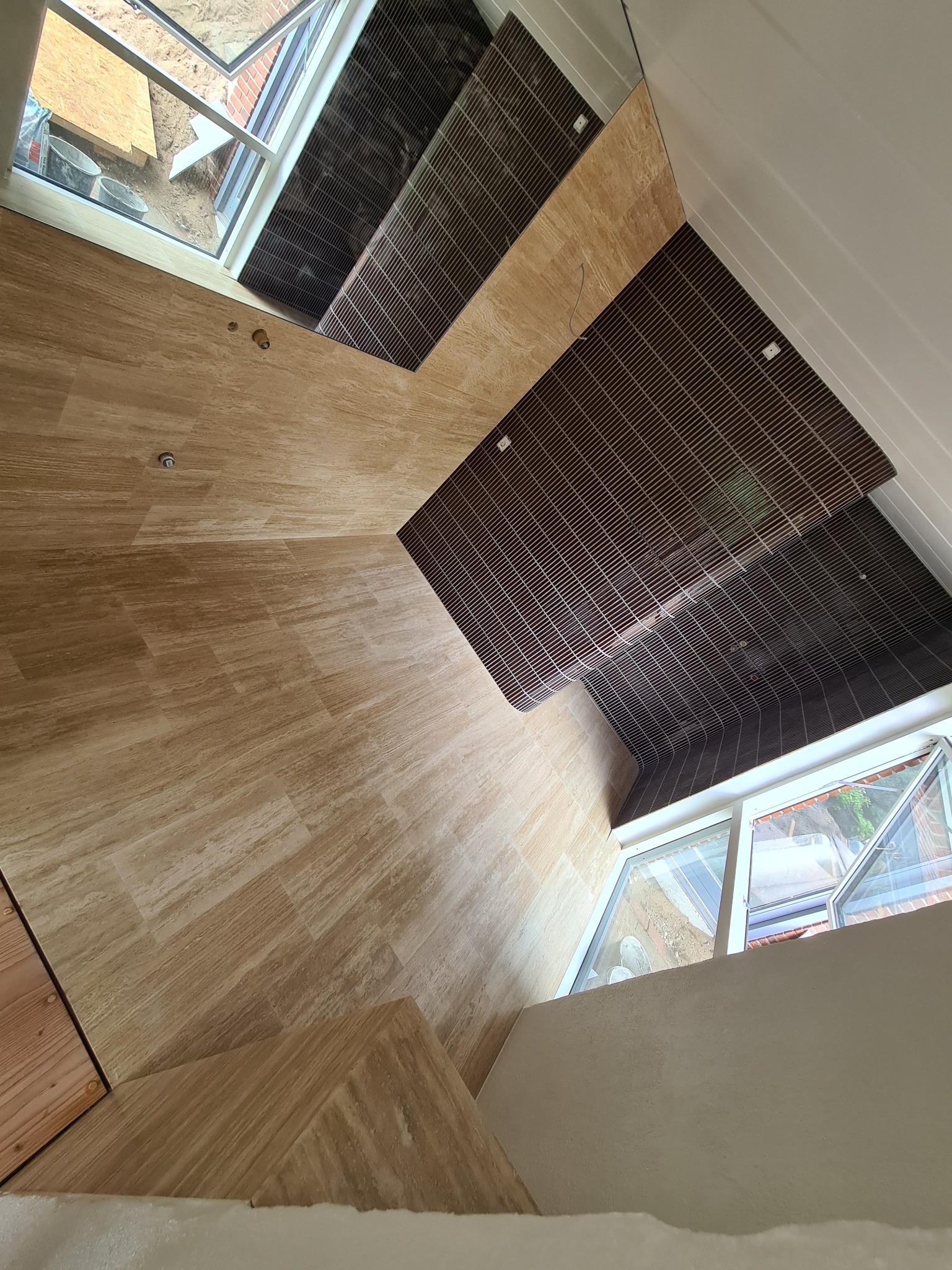 Ukończona łazienka z beżowymi płytkami imitującymi drewno na podłodze i ścianach, oraz ciemnymi panelami na suficie. Widoczne okno dachowe i fragment okna.