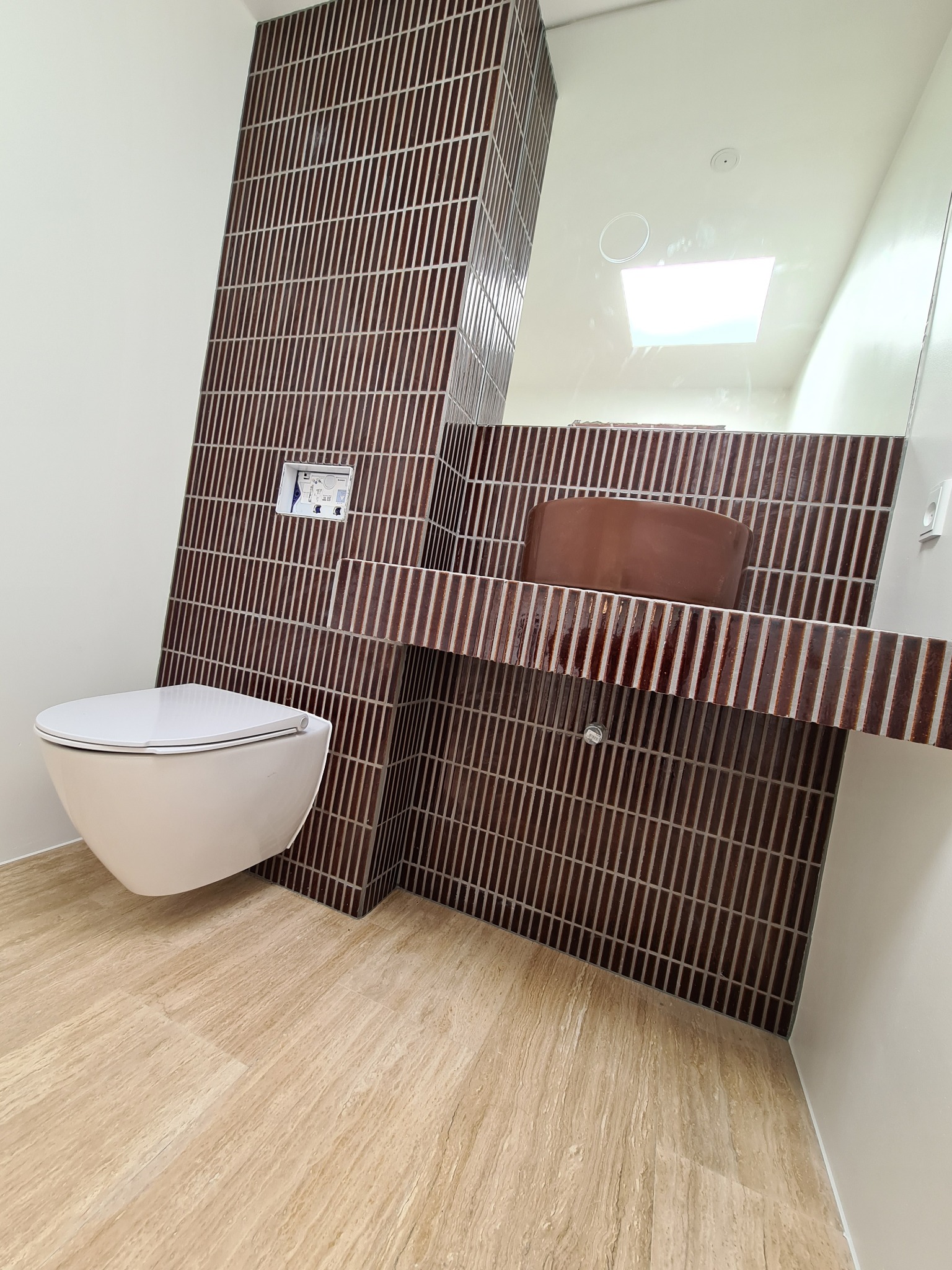 Nowoczesna łazienka w Mstowie z brązowymi płytkami ułożonymi pionowo, podwieszana toaleta i umywalka. Minimalistyczny design i jasna podłoga.